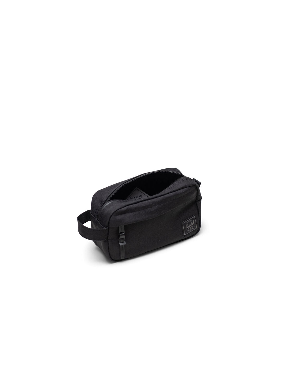 The Herschel Chapter Small Travel Kit is a black rectangular, eco-friendly toiletry bag with a side handle, zippered opening, and a small rectangular logo patch on the front, shown against a plain white background.