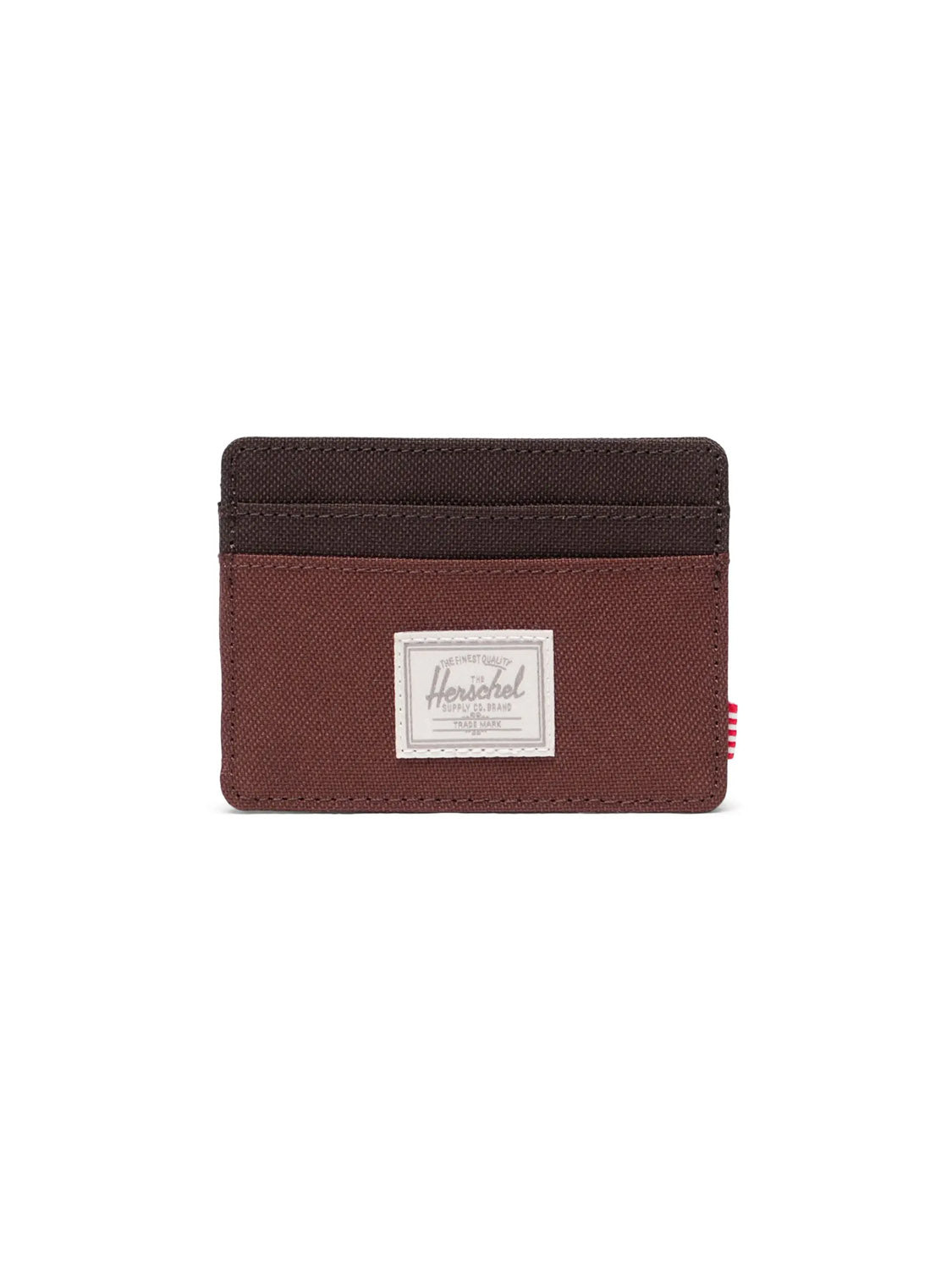 The Herschel Charlie Cardholder Wallet is a slim brown and dark brown RFID-blocking card holder with multiple slots, a white rectangular Herschel label on the front, and a red and white striped tab on the side.