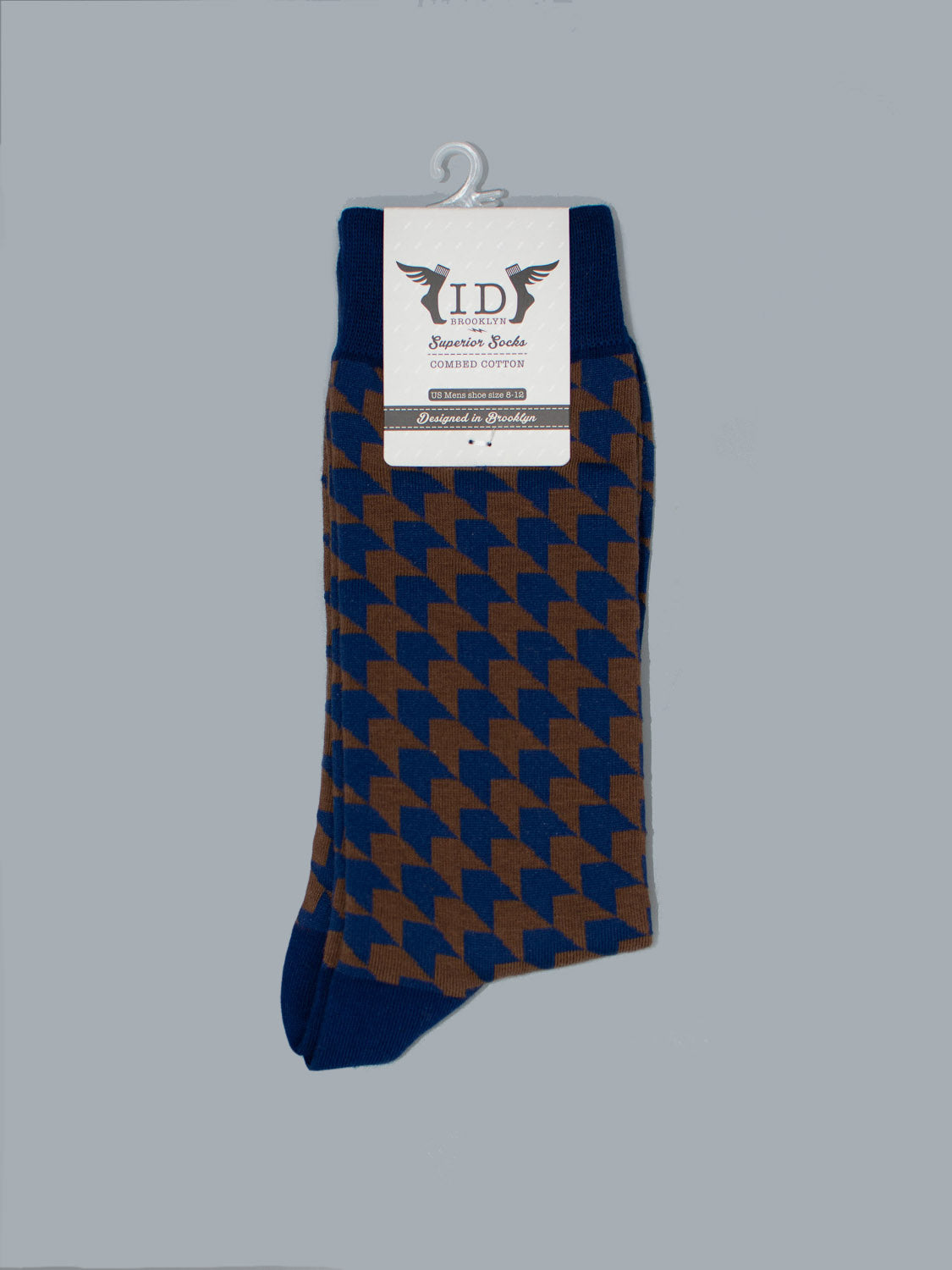 A pair of Check Graphic Socks by ID Menswear, featuring a blue and brown houndstooth pattern in soft combed cotton, is shown against a gray background with a white label displaying the brand name and mens shoe size 8-12 on a plastic hanger.