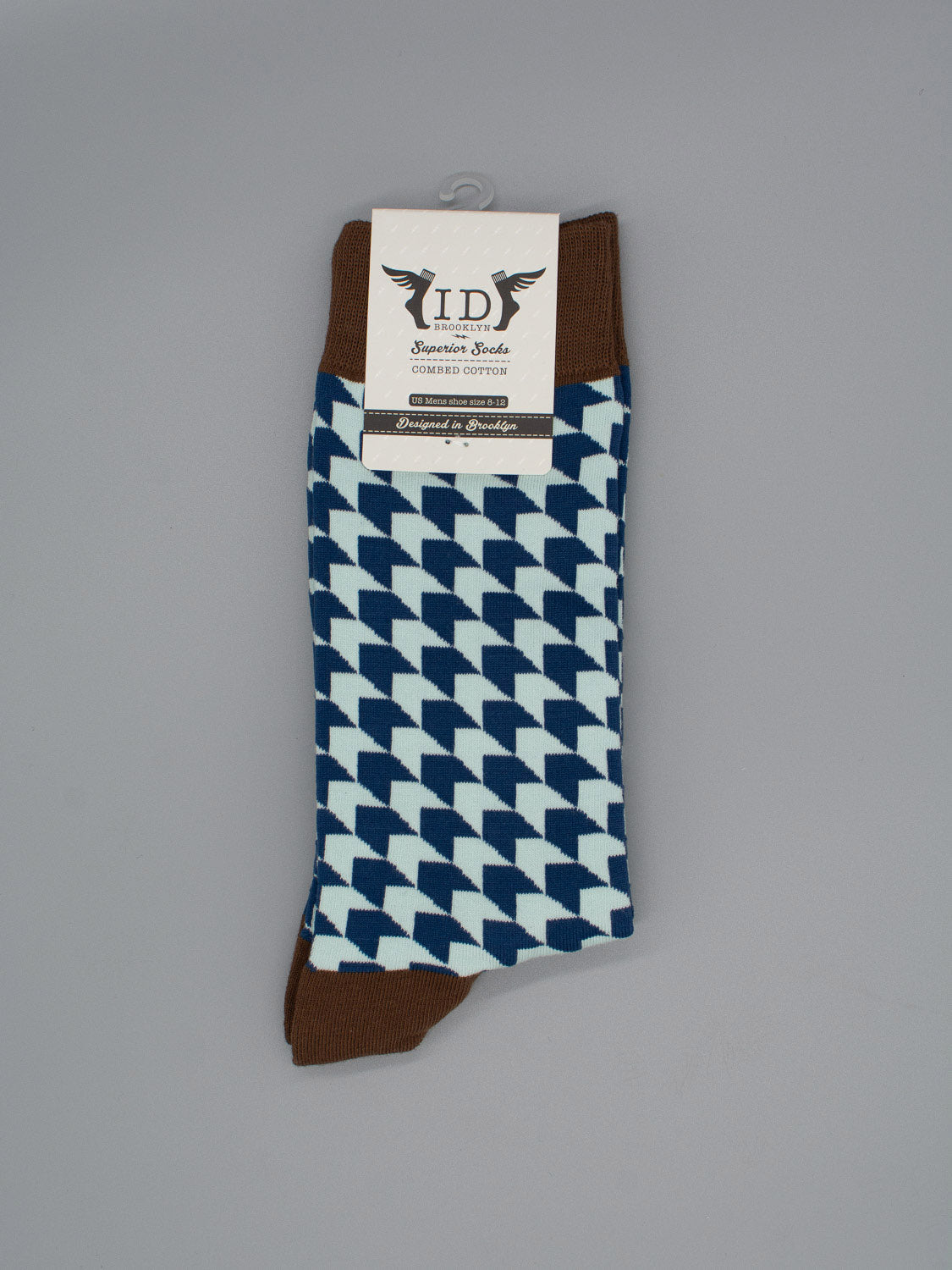 A pair of Check Graphic Socks by ID Menswear, featuring blue and white geometric patterns with brown cuffs, heels, and toes. Made from soft combed cotton and shown against a plain gray background with a branded label at the top.