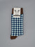 A pair of Check Graphic Socks by ID Menswear, featuring blue and white geometric patterns with brown cuffs, heels, and toes. Made from soft combed cotton and shown against a plain gray background with a branded label at the top.