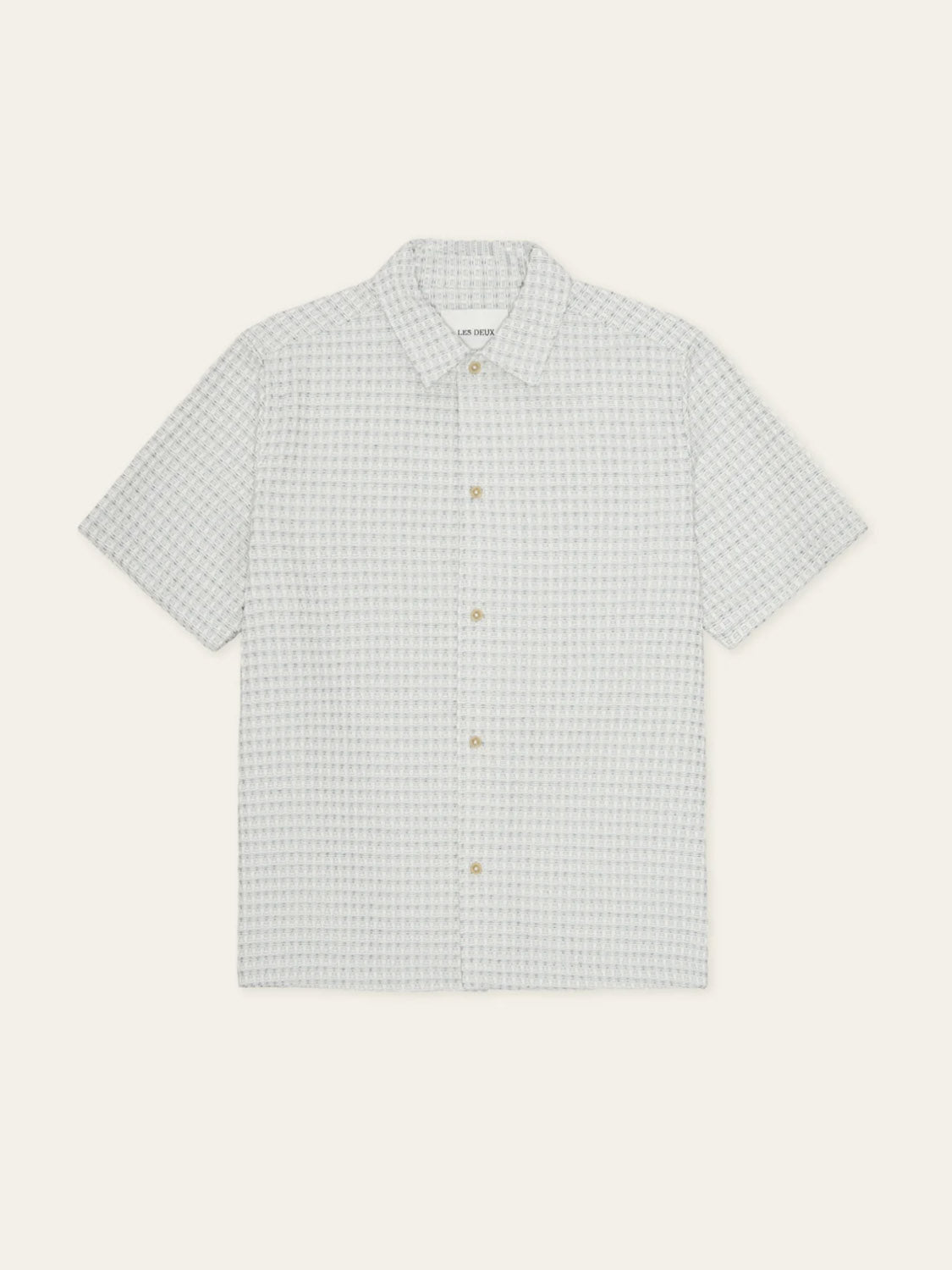 The Les Deux Check Seersucker SS Shirt features short sleeves, a light gray and white small check pattern, a pointed collar, and beige buttons, displayed laid flat on a plain light background.