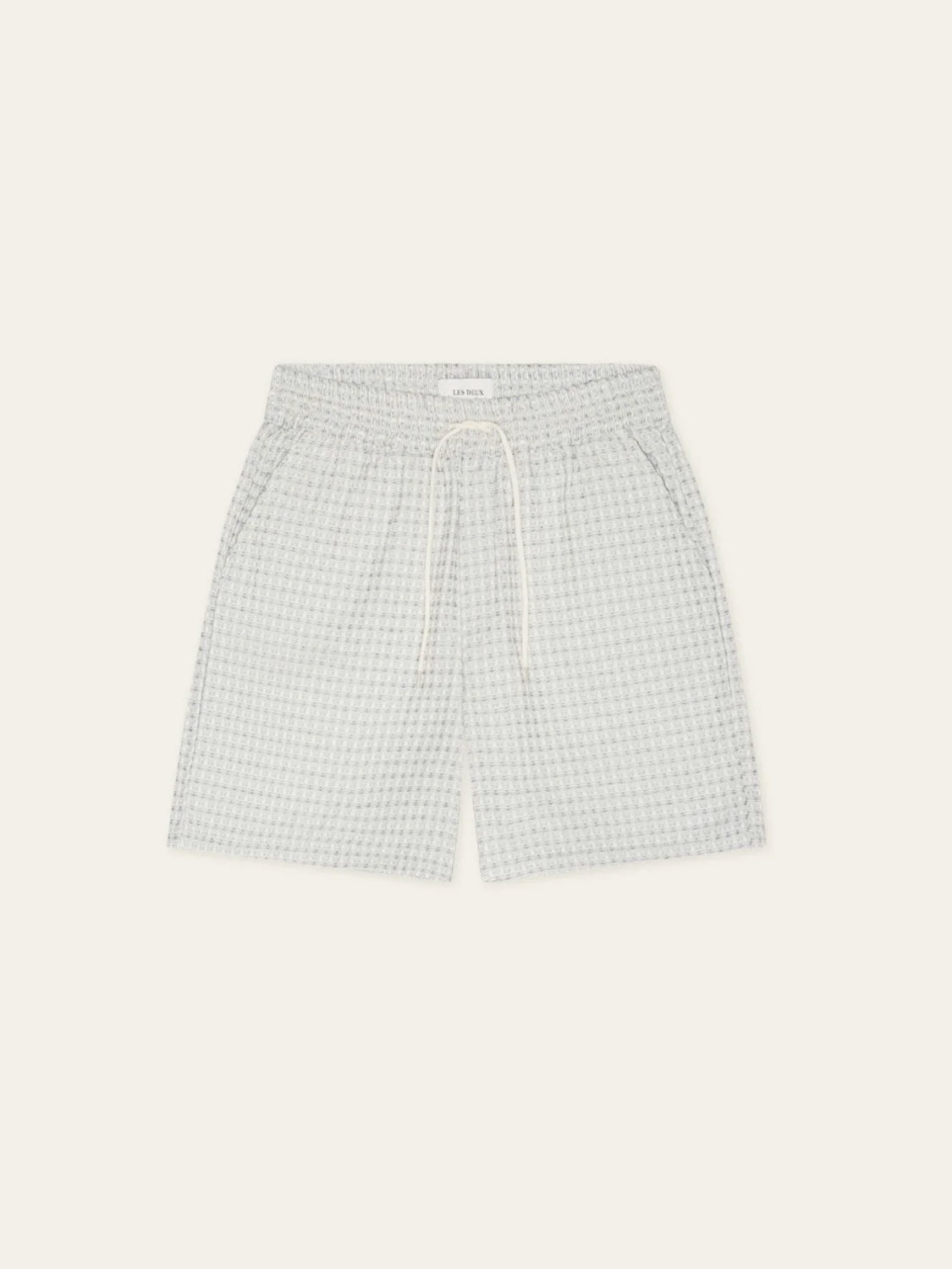 Les Deux Check Seersucker Shorts in light grey and white cotton with an elastic waistband, white drawstring, and side pockets, shown on a plain off-white background.