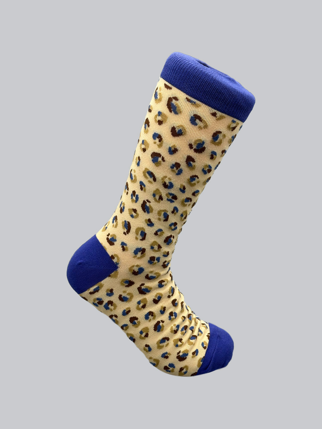 The Cheetah Graphic Sock from ID Menswear is a mens sock made of combed cotton with a beige base and black-brown cheetah print. It features a solid dark blue toe, heel, and cuff, all set against a light gray background.