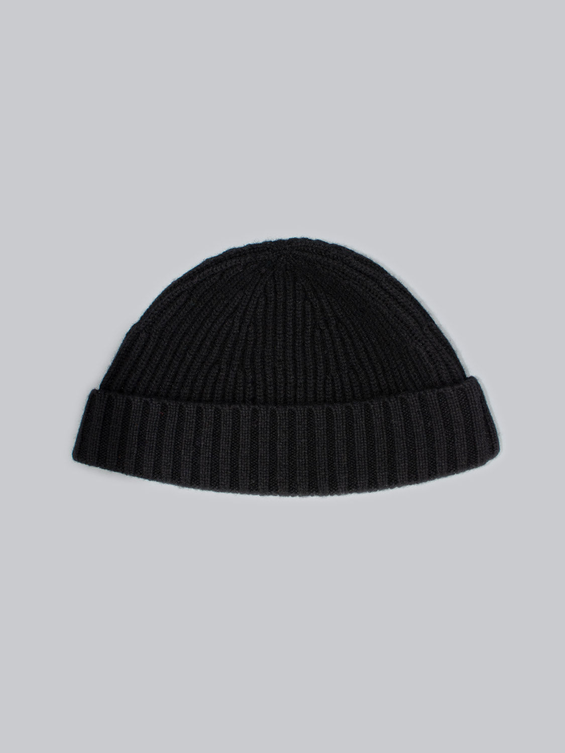 Introducing the Cho Oyu Merino Wool Fishermans Beanie by ID Menswear, a black ribbed knit hat with a folded brim. Centered on a light gray backdrop, this classic winter accessory is crafted from luxurious merino wool to highlight its timeless design.