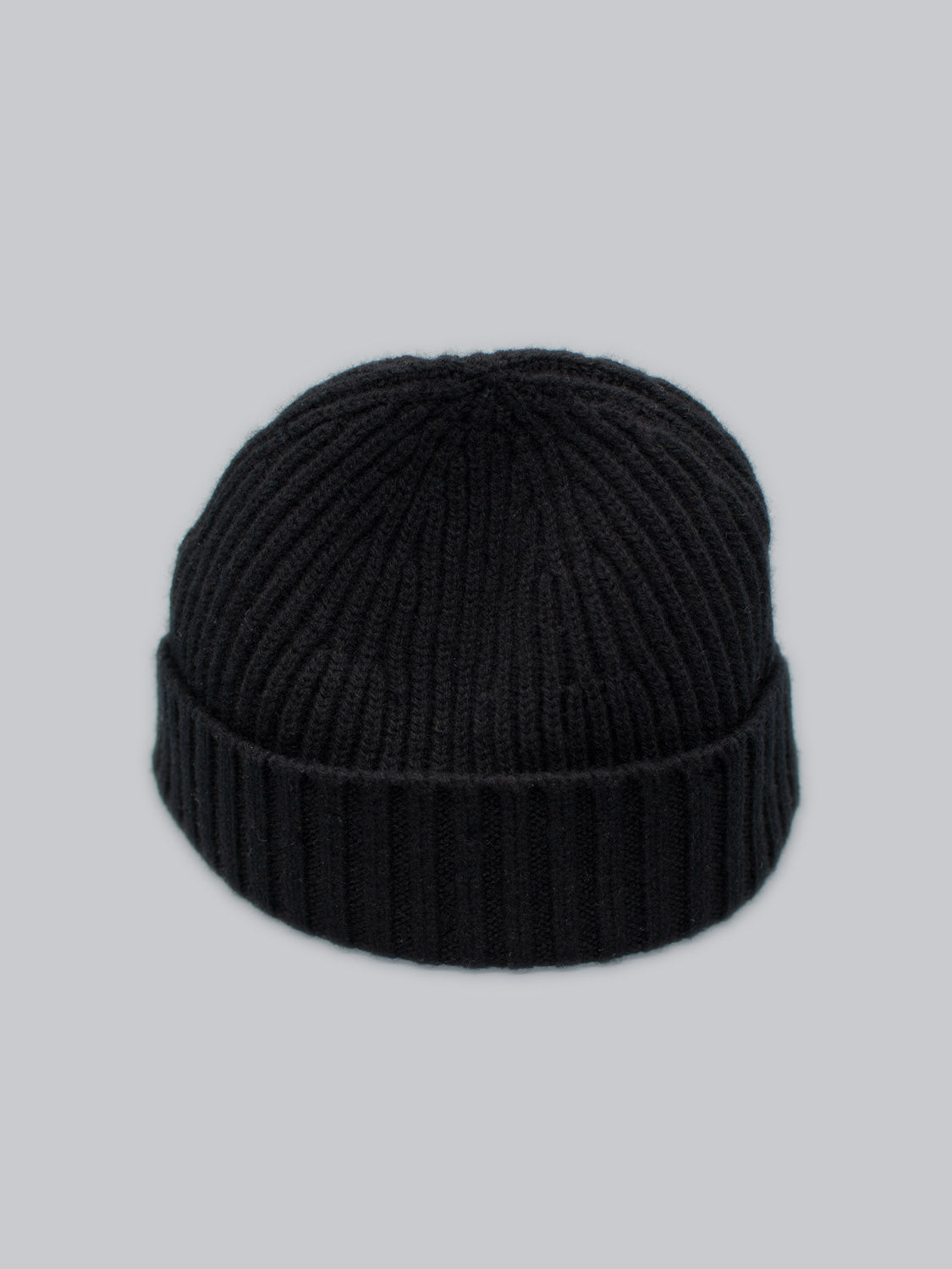 The Cho Oyu Merino Wool Fishermans Beanie by ID Menswear is a black knit beanie with ribbed texture, made from cozy merino wool, shown on a light gray background. This stylish winter accessory is ideal for chilly days.