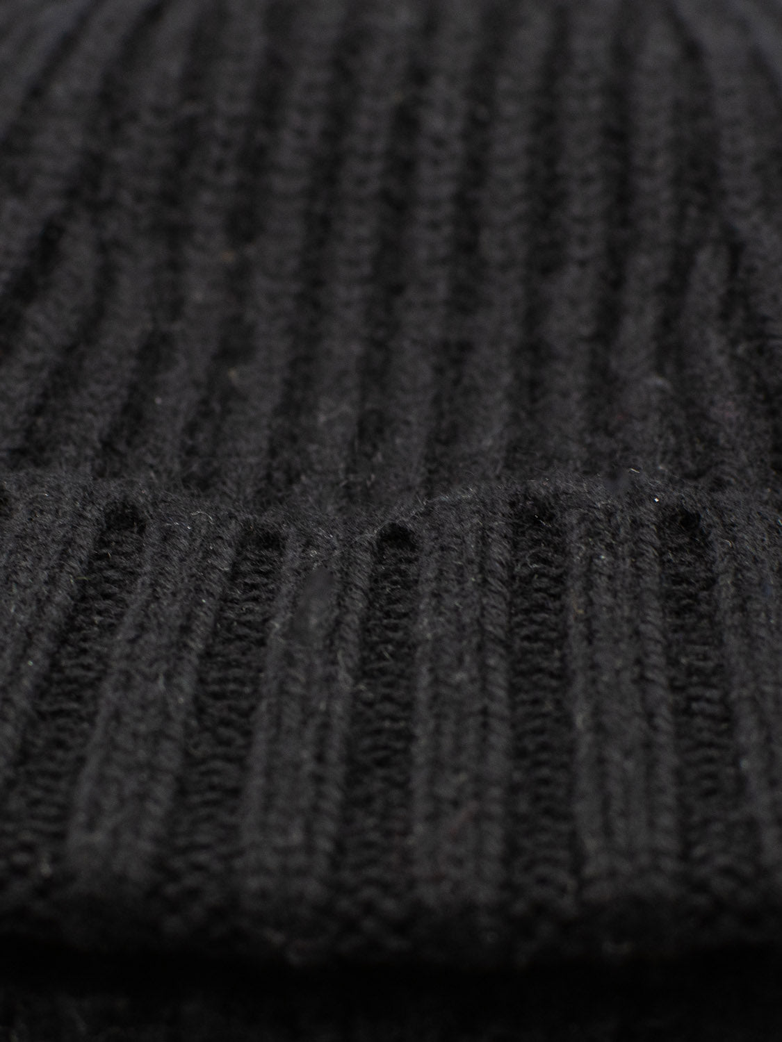 Close-up of a black knit fabric with vertical ribbing, similar to the intricate pattern of an ID Menswear Cho Oyu Merino Wool Fishermans Beanie, highlighting its deep black hue and evoking the cozy essence of a winter accessory.