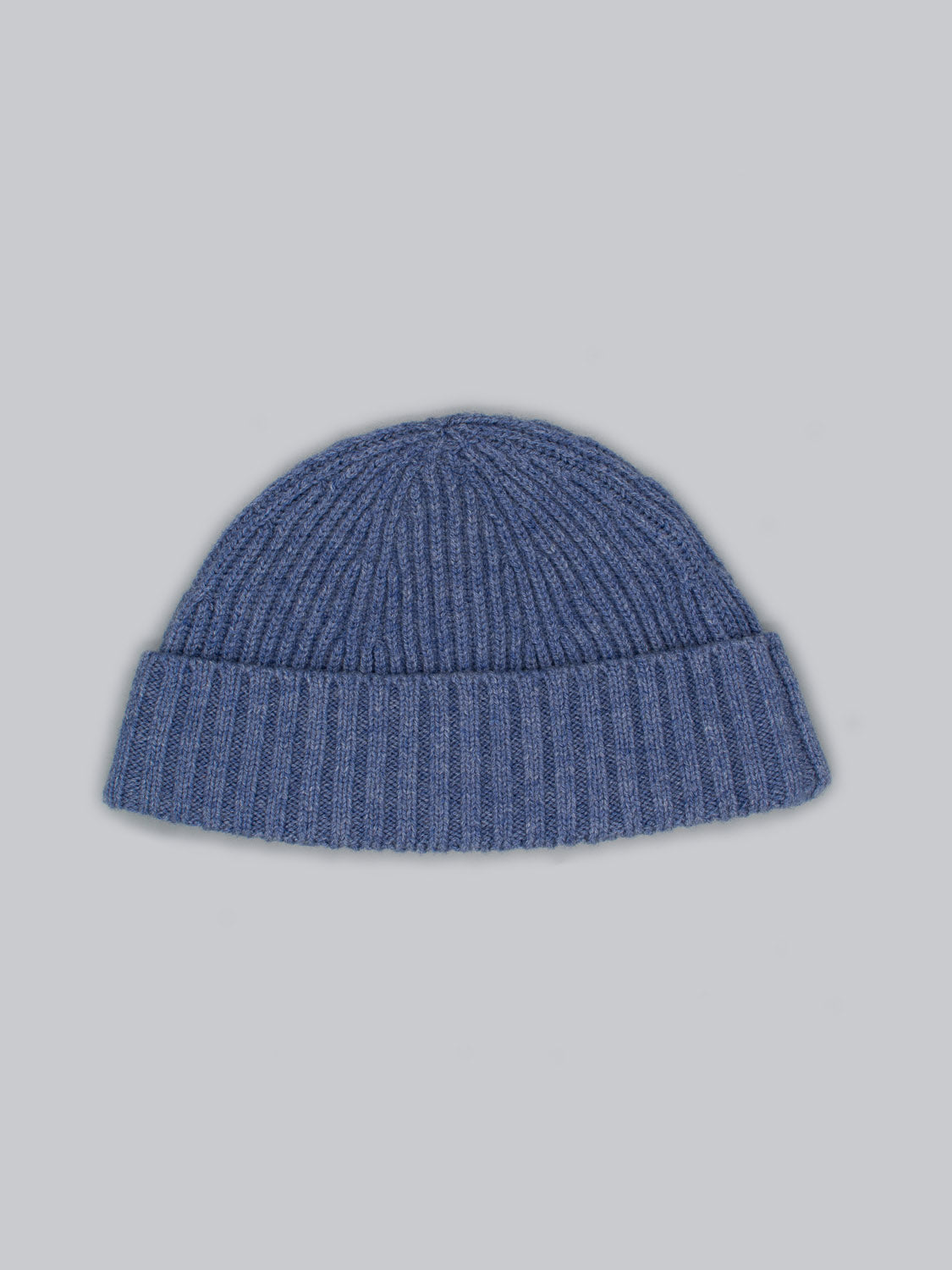 The Cho Oyu Merino Wool Fishermans Beanie by ID Menswear is a blue knitted piece featuring a ribbed texture and folded brim, ideal for winter, displayed against a light gray background.