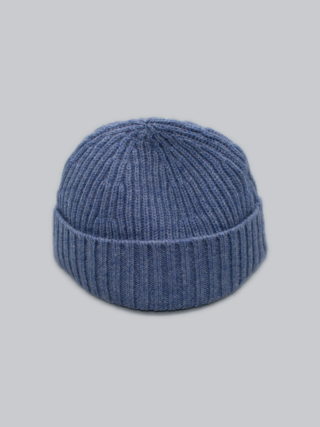 The Cho Oyu Merino Wool Fishermans Beanie by ID Menswear, in blue with a folded brim against a plain gray background, is the perfect winter accessory.
