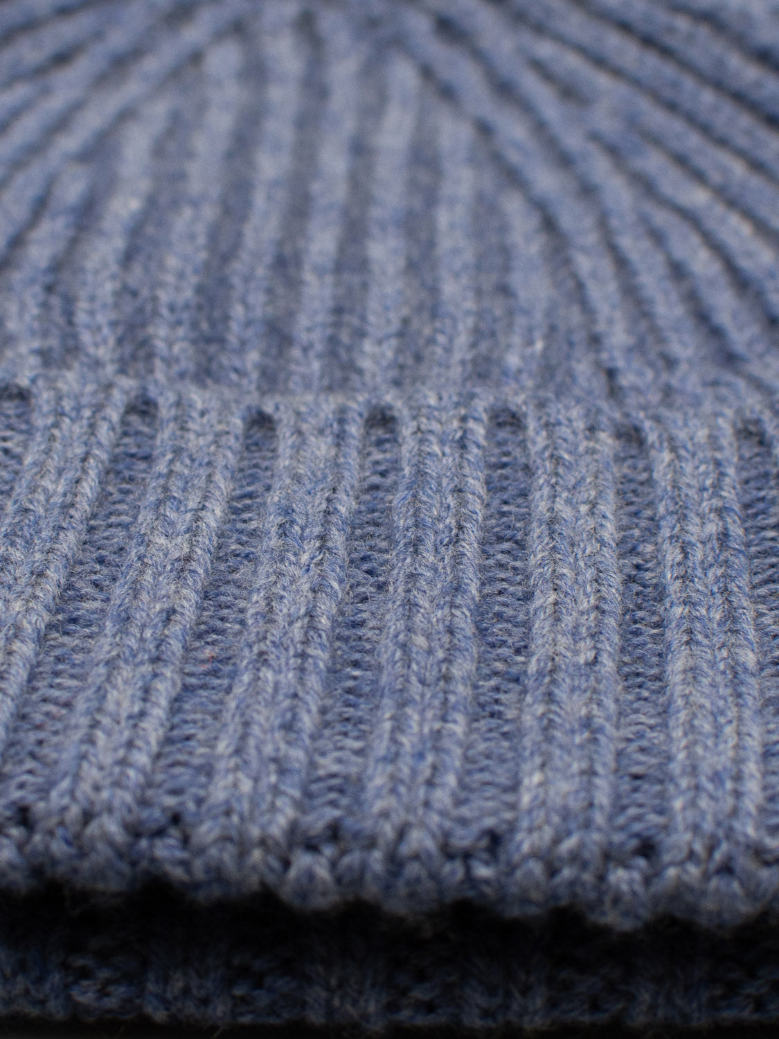 Close-up of a blue, ribbed-knit fabric highlights its soft, woven texture. The thick, warm material, often used in winter accessories like beanies or sweaters, is perfect for styles such as the Cho Oyu Merino Wool Fishermans Beanie by ID Menswear.