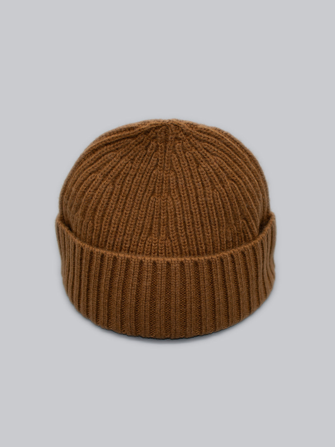 A cozy brown Cho Oyu Merino Wool Fishermans Beanie by ID Menswear, featuring ribbed knit and a folded cuff, perfect for your winter wardrobe, displayed against a light gray background.