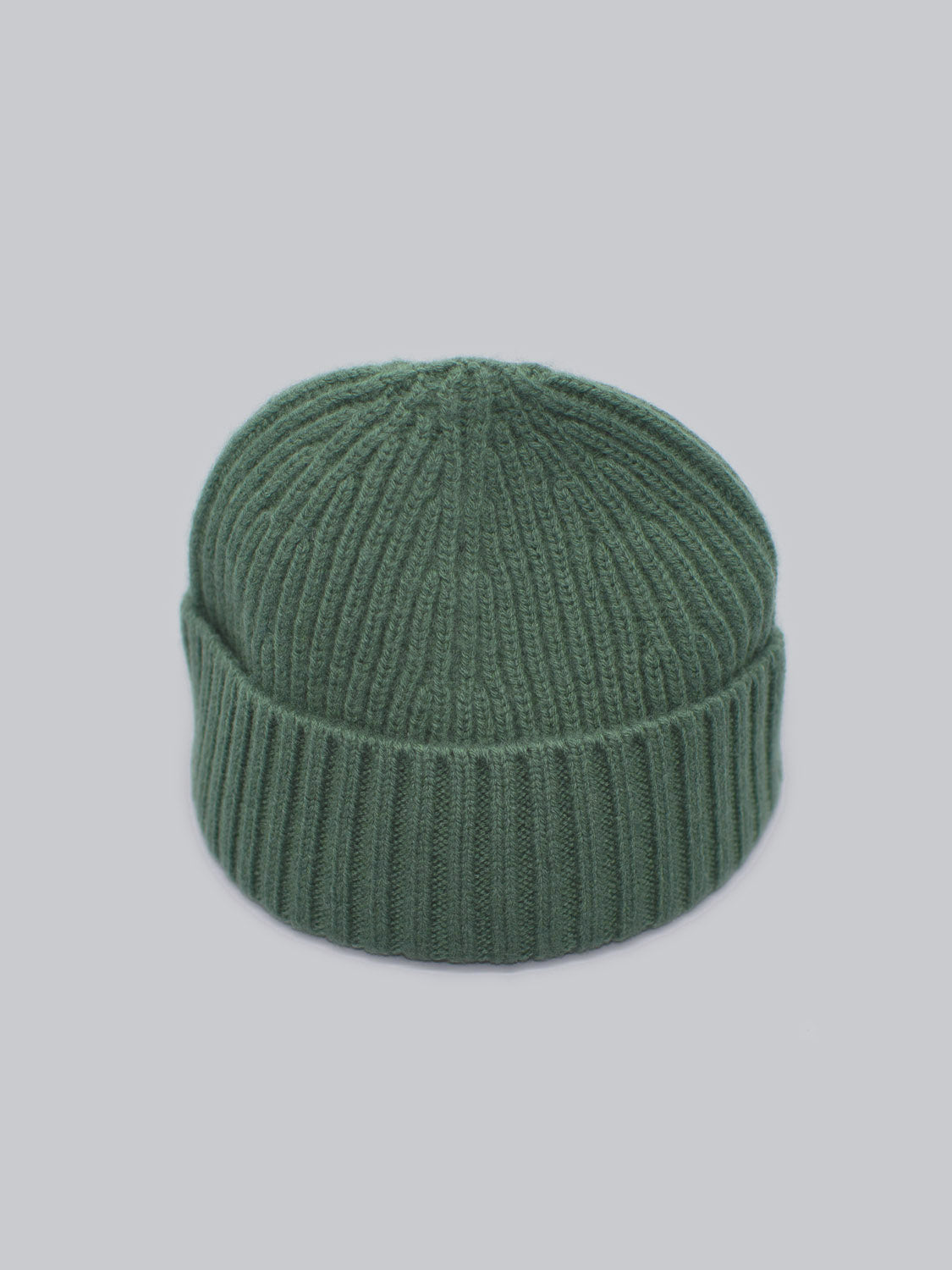 The Cho Oyu Merino Wool Fishermans Beanie by ID Menswear, a green merino wool accessory with a ribbed pattern, is perfect for winter and set against a light gray background.