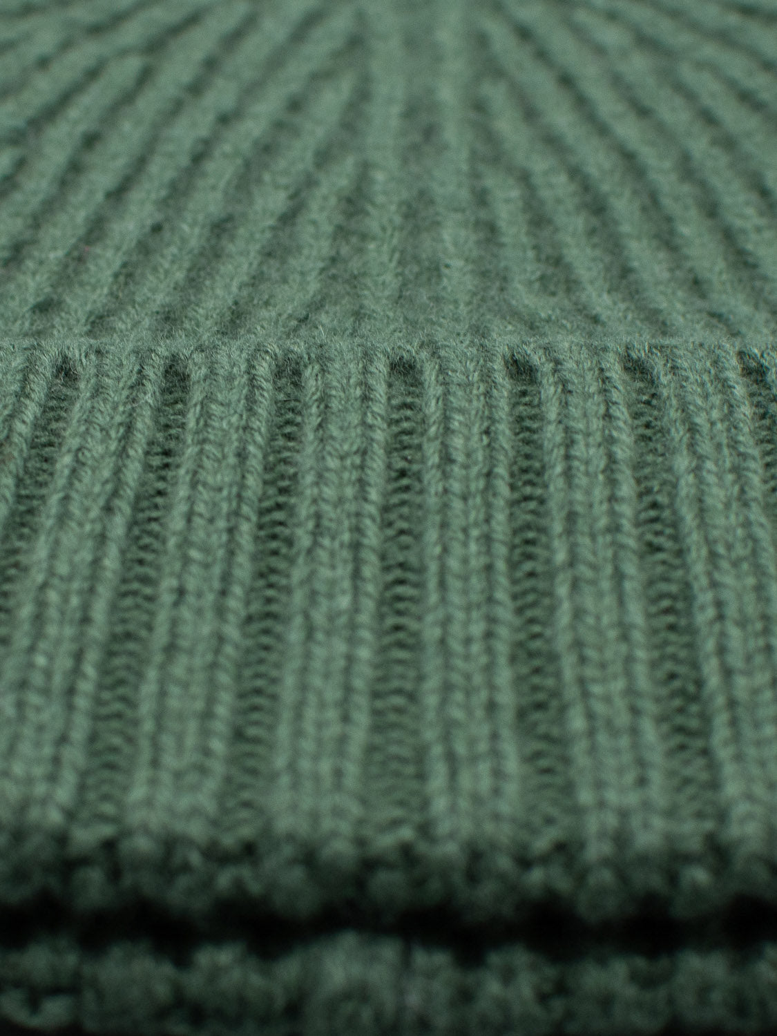 Close-up of a green merino wool fabric with ribbed texture. This winter accessory from ID Menswear highlights the intricate vertical ribbing, similar to the Cho Oyu Merino Wool Fishermans Beanie.