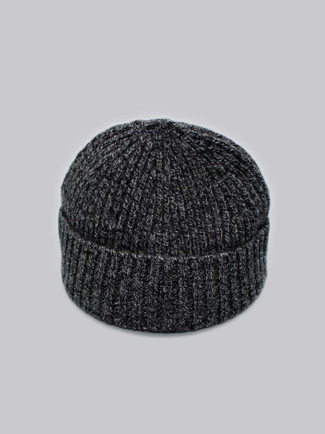The Cho Oyu Merino Wool Fishermans Beanie from ID Menswear is a dark gray beanie with a folded brim, ideal as a winter accessory against a light gray background.