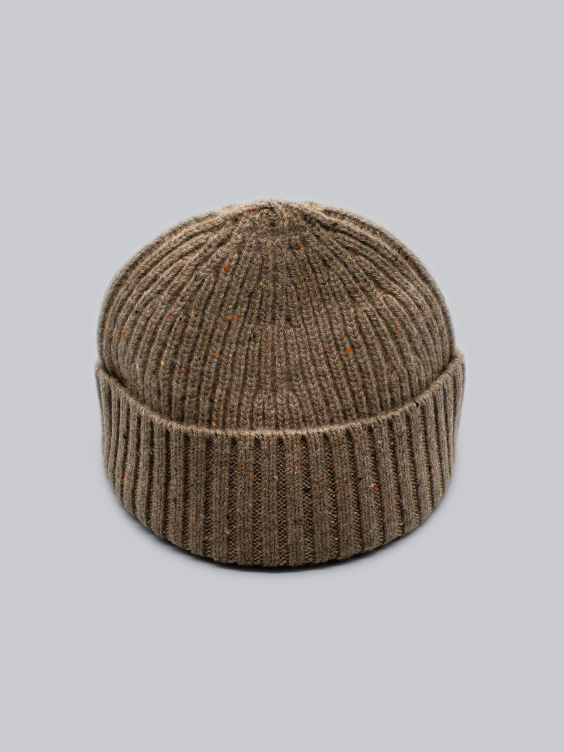 The Cho Oyu Merino Wool Fishermans Beanie by ID Menswear, featuring a brown hue with subtle orange specks and a folded brim, is showcased against a plain gray background.
