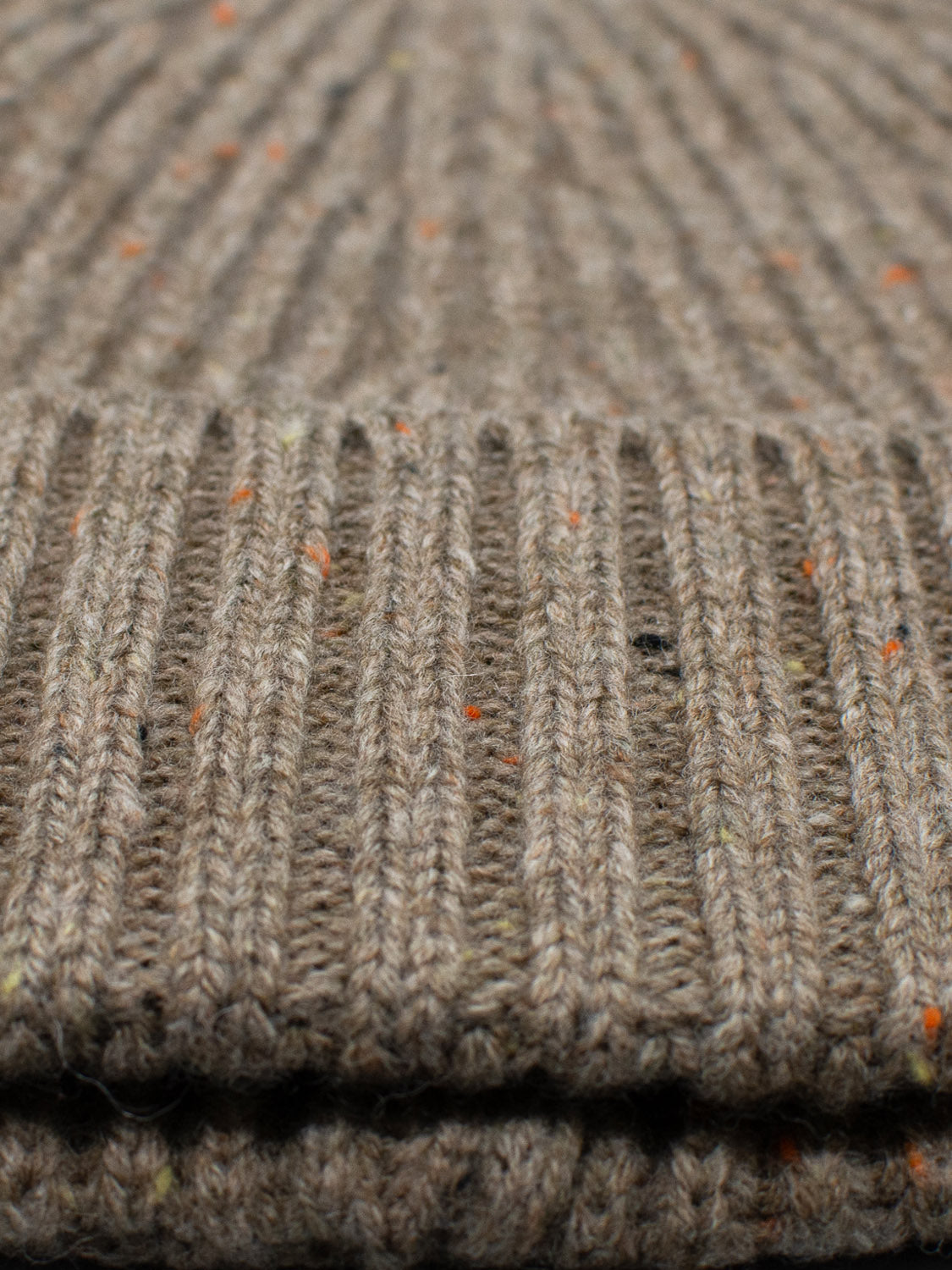 Close-up of ID Menswears Cho Oyu Merino Wool Fishermans Beanie, showcasing a ribbed, brown fabric with orange, yellow, and black speckles. This thick knit ensures warmth and coziness, making it perfect for winter wear.