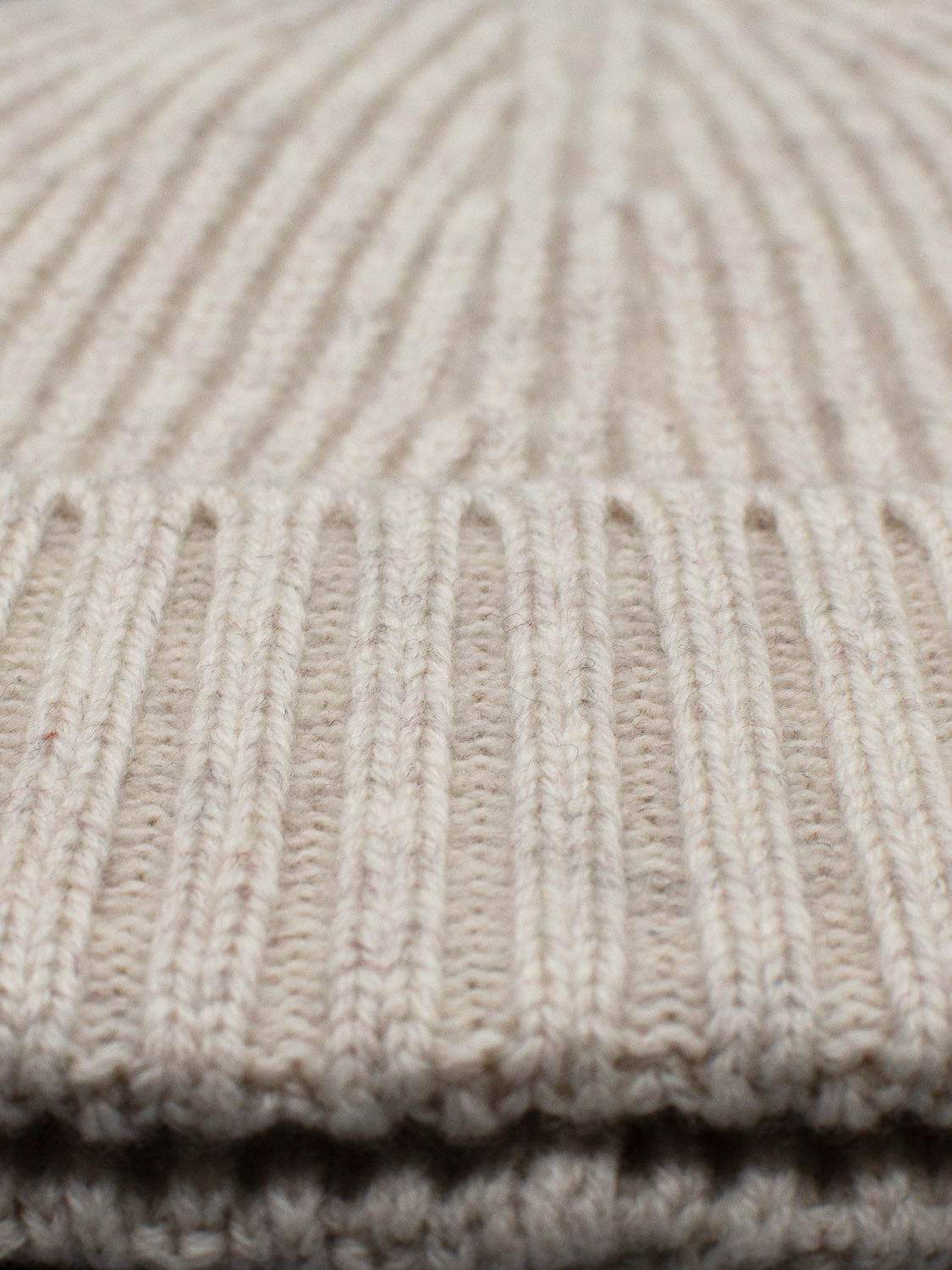 Close-up of a beige knit fabric with a ribbed pattern reminiscent of the Cho Oyu Merino Wool Fishermans Beanie by ID Menswear. The texture showcases parallel lines and a soft, cozy feel, perfect for enhancing your winter wardrobe.