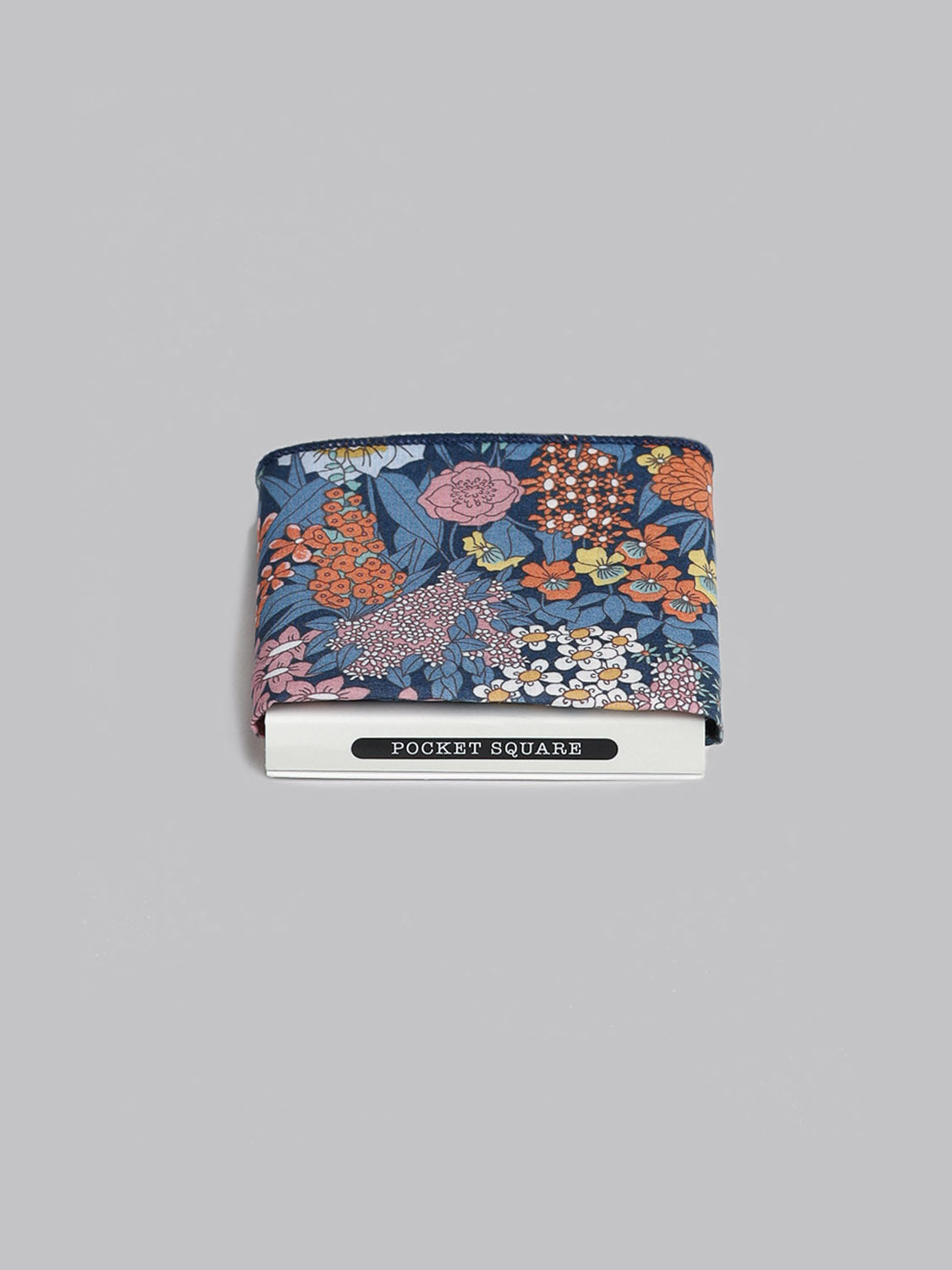 A folded Liberty™ Ciara Pocket Square by ID Menswear, made from soft Tana Lawn cotton, displays a blue, orange, pink, and white floral pattern on gray above a white Pocket Square label.