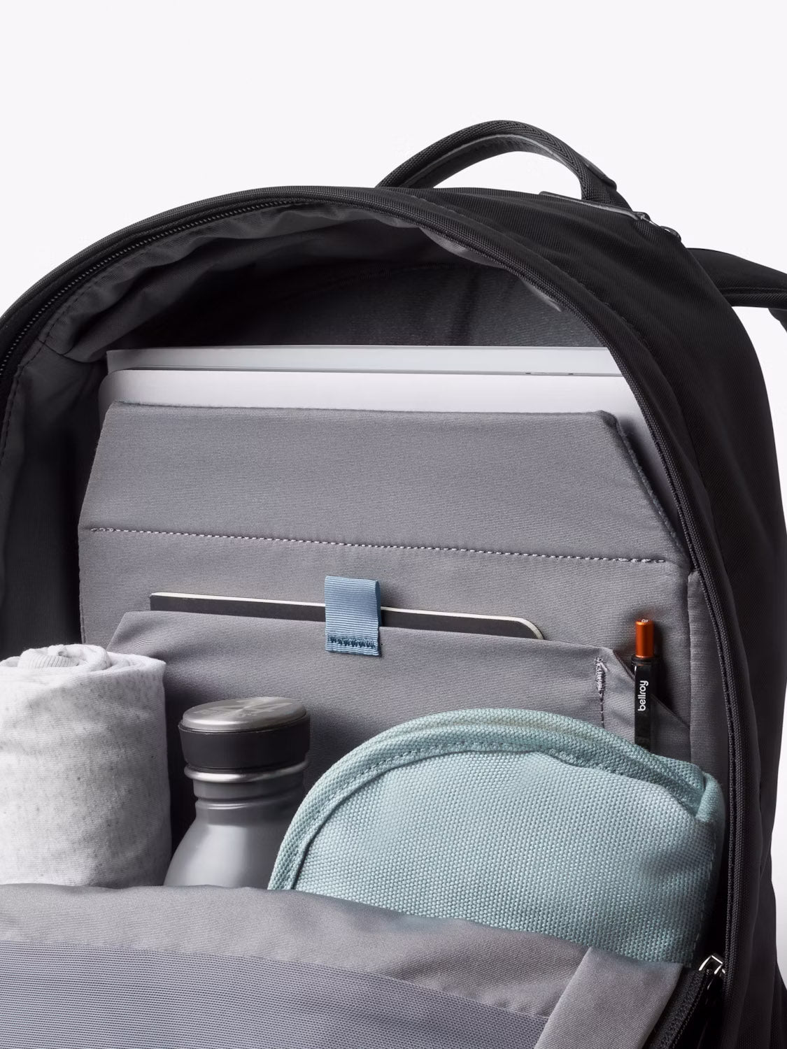 The Bellroy Classic Compact Backpack - 16L is shown open, neatly organizing a laptop, tablet, rolled-up gray shirt, gray water bottle, teal pouch, and pens in dedicated pockets.