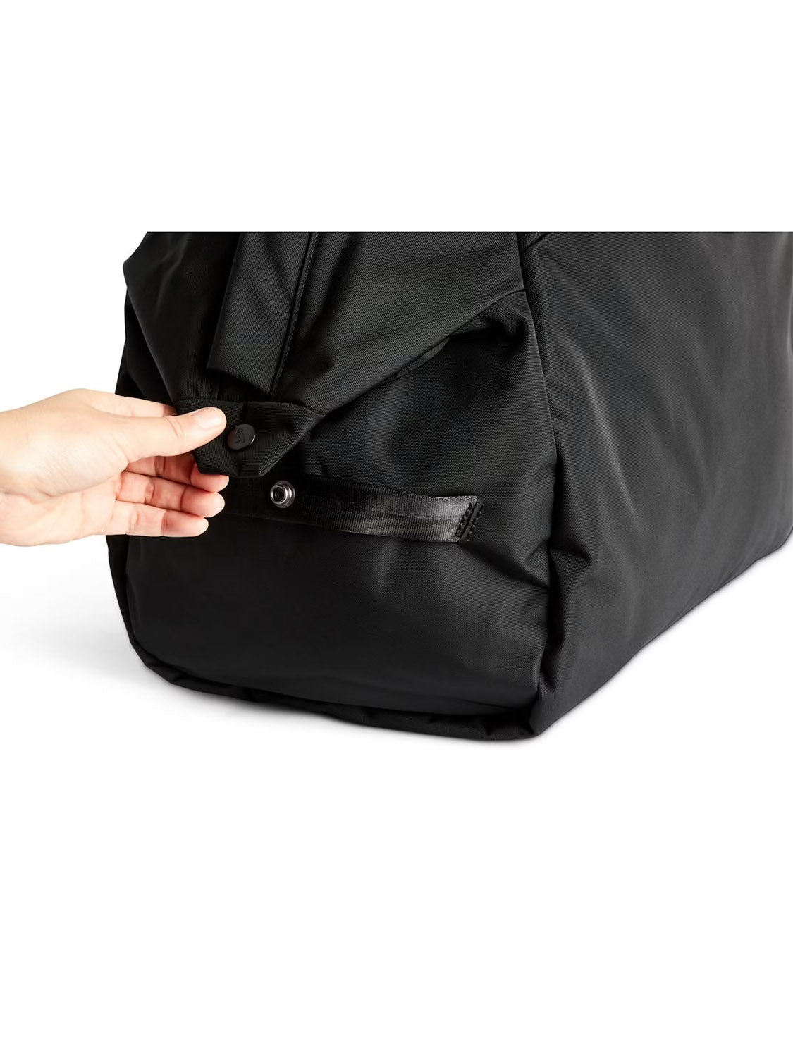A hand opens a buttoned flap on the corner of the Bellroy Classic Weekender Duffle Bag - 45L, made of smooth black fabric.