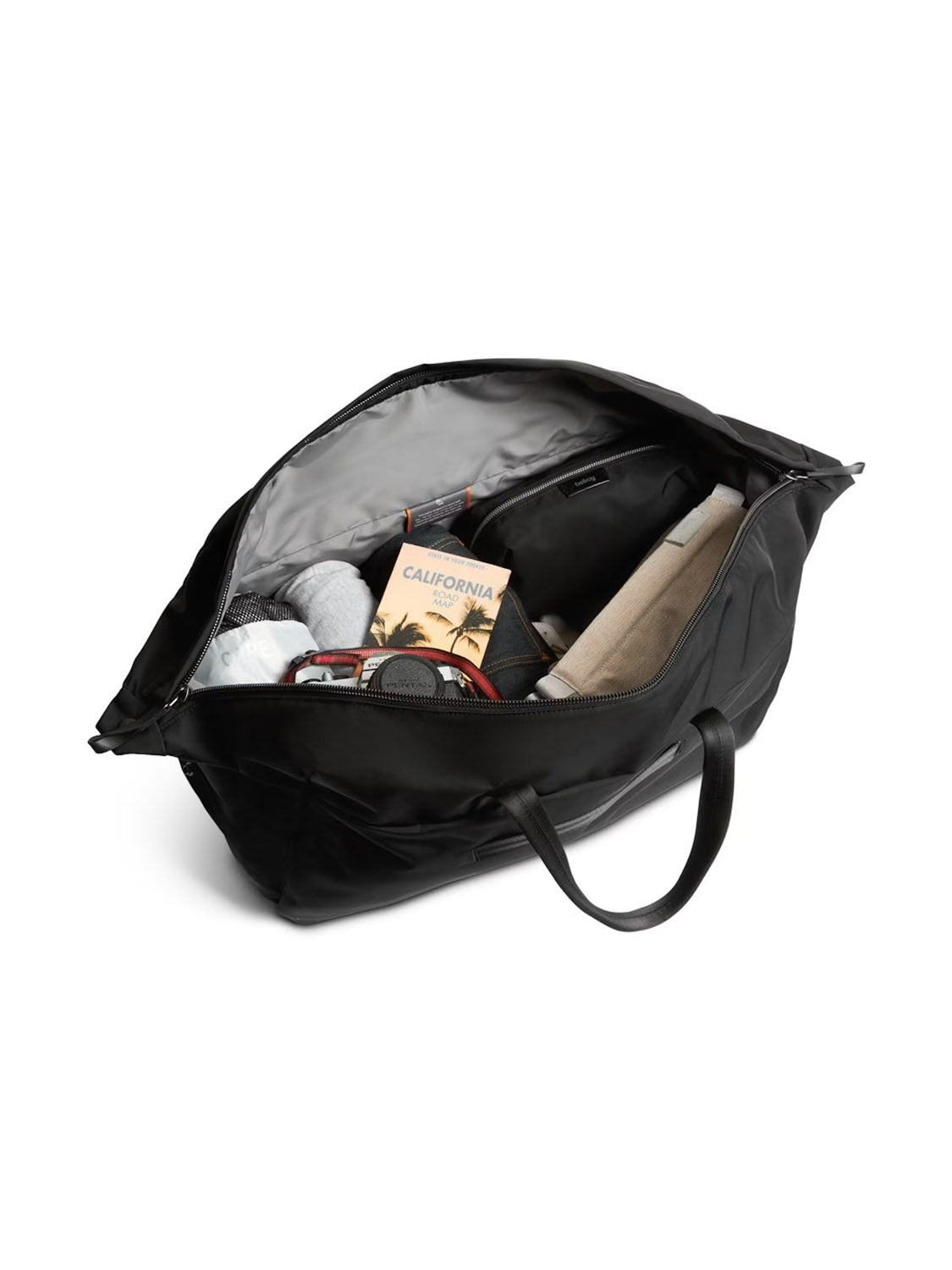 A Bellroy Classic Weekender Duffle Bag - 45L is unzipped to reveal its neatly packed contents, including a rolled towel, a book titled California, clothes, and other travel essentials.