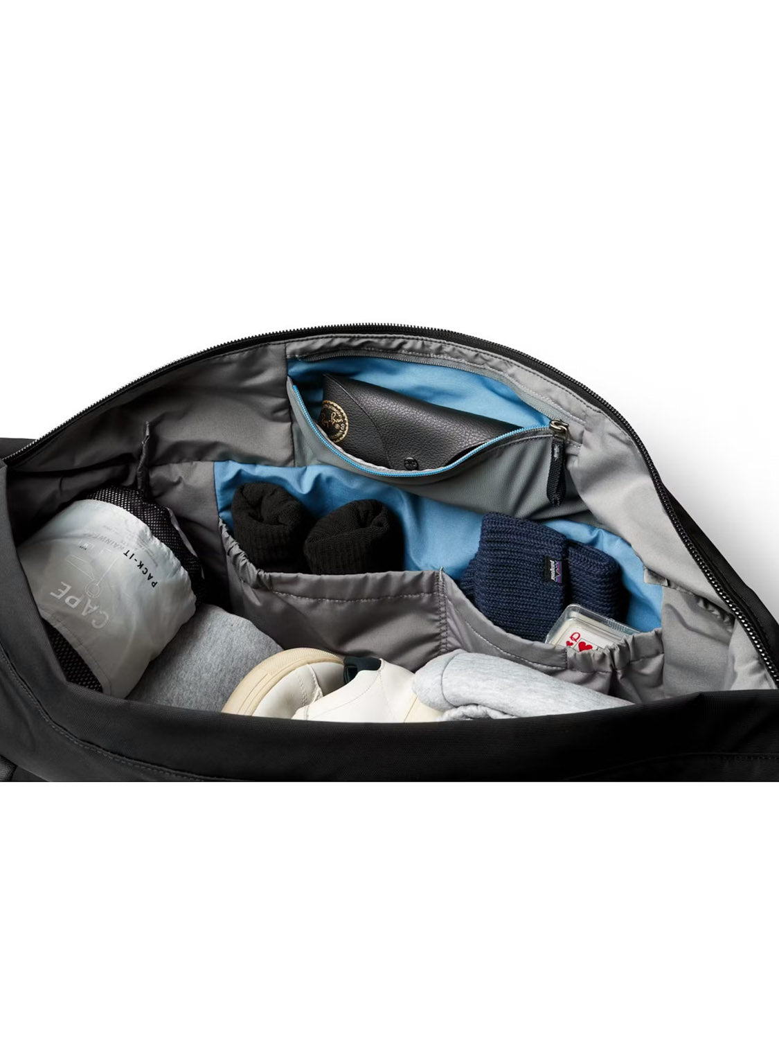 The Bellroy Classic Weekender Duffle Bag - 45L is shown neatly packed with folded clothes, sneakers, socks, and a cap. Small items fit in zippered mesh pockets. The organized interior is partially lined light blue and includes a luggage pass-through.
