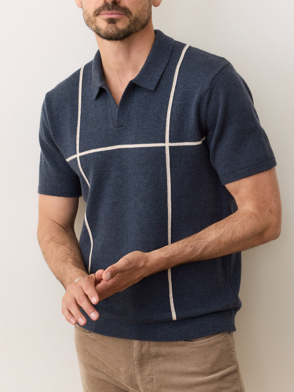 A man wears the Marine Layer Cliff Sweater Polo—navy blue with white grid lines—and beige pants, standing against a light background. His face is partially out of frame.