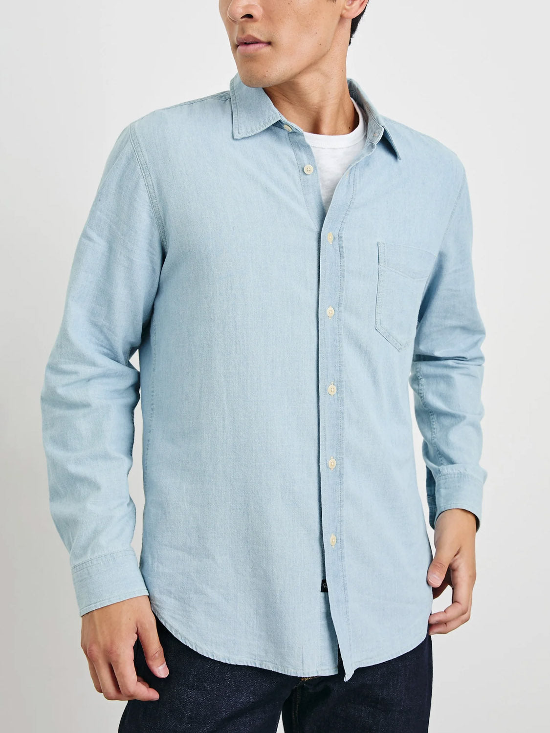 Wearing a Rails Colton Dark Wash Indigo Shirt, this person pairs it with dark jeans. They stand casually against a plain white backdrop, their face slightly turned to the side.