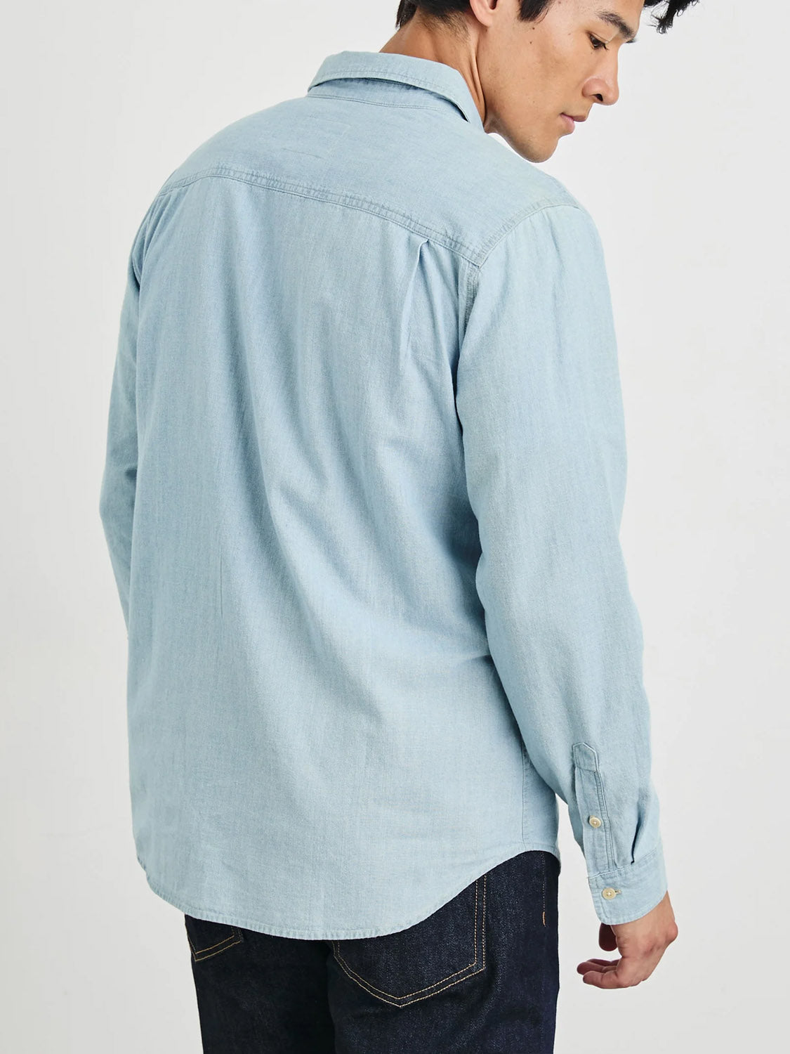 A man in a Rails Colton Dark Wash Indigo Shirt and dark jeans stands with his back to the camera, casting a glance over his shoulder.