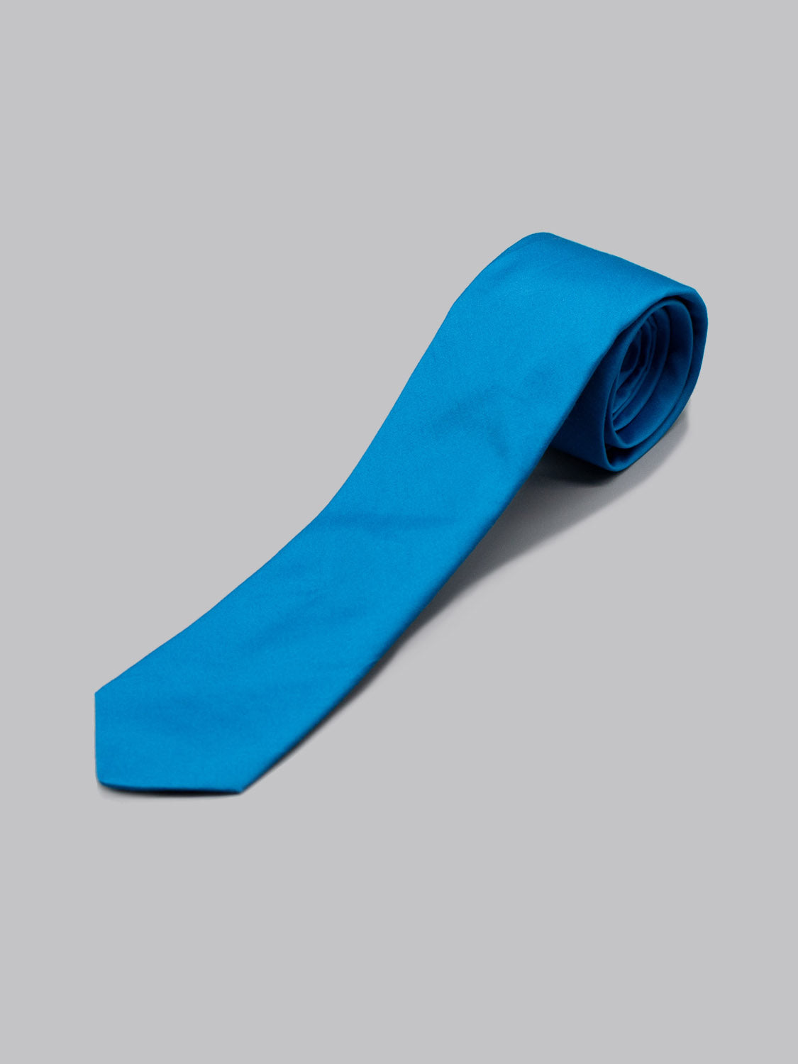 The Blue Jay Cotton Tie by ID Menswear, handmade in Brooklyn from 100% cotton, is shown rolled up in bright blue on a plain light gray background.