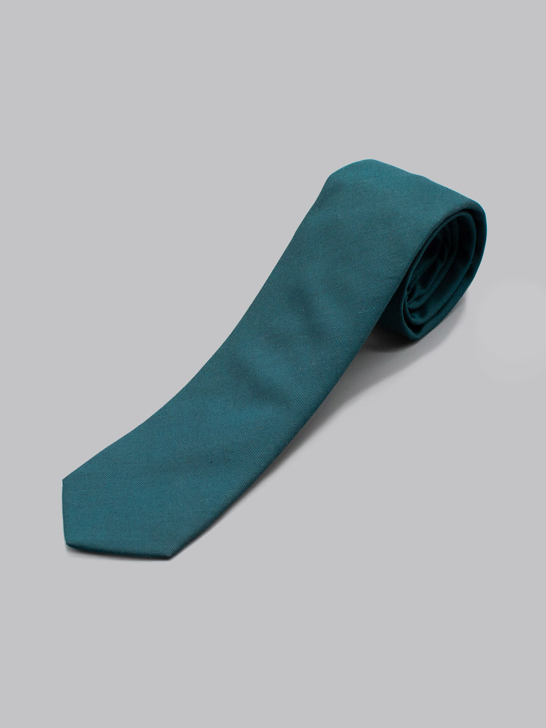 The Emerald Cotton Tie by ID Menswear, handmade from cotton in Brooklyn, is neatly rolled at one end and displayed on a plain light gray background.