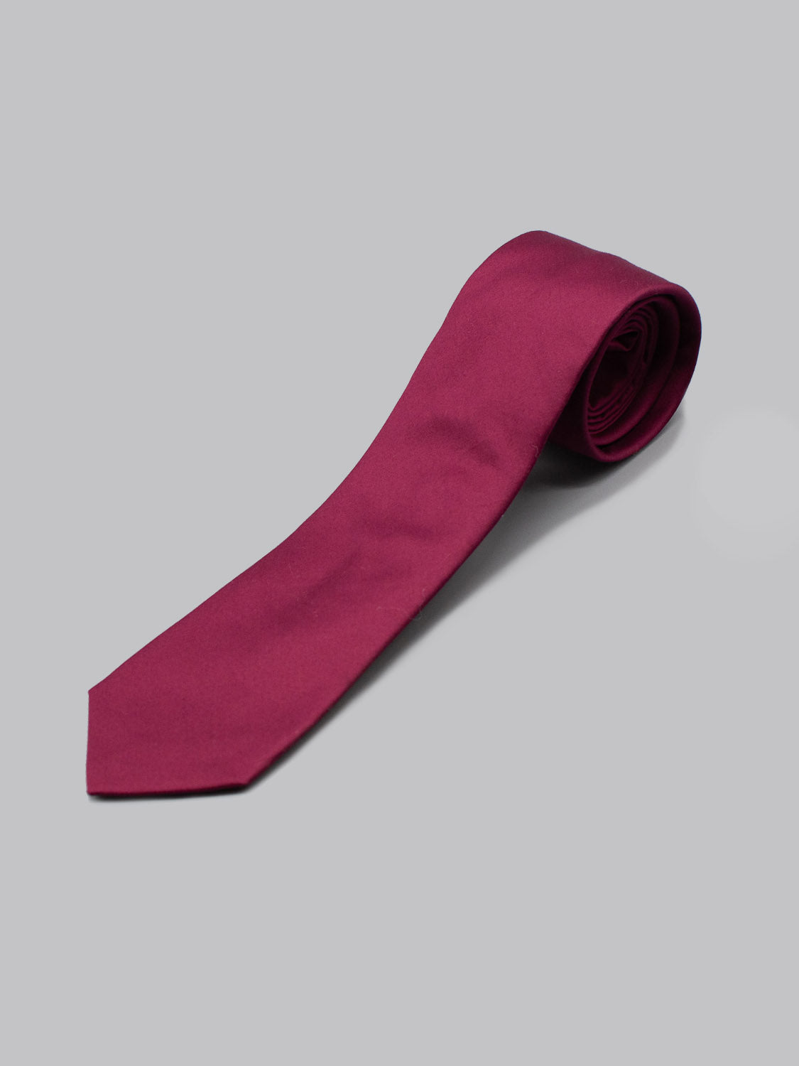 A handmade, rolled-up ID Menswear Egyptian Firefinch Cotton Tie in solid magenta is displayed on a plain light gray background.