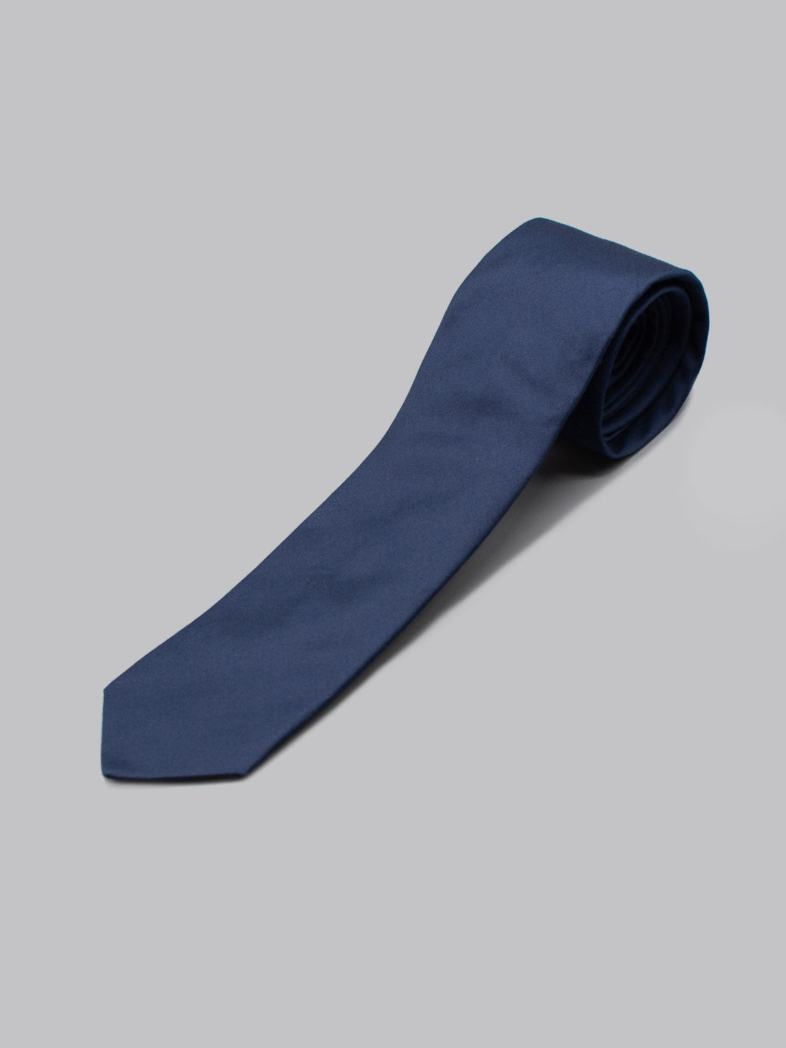 The Indigo Cotton Tie by ID Menswear, handmade in Brooklyn from solid navy blue cotton, is neatly rolled and displayed on a light gray background—ideal for business formal occasions.