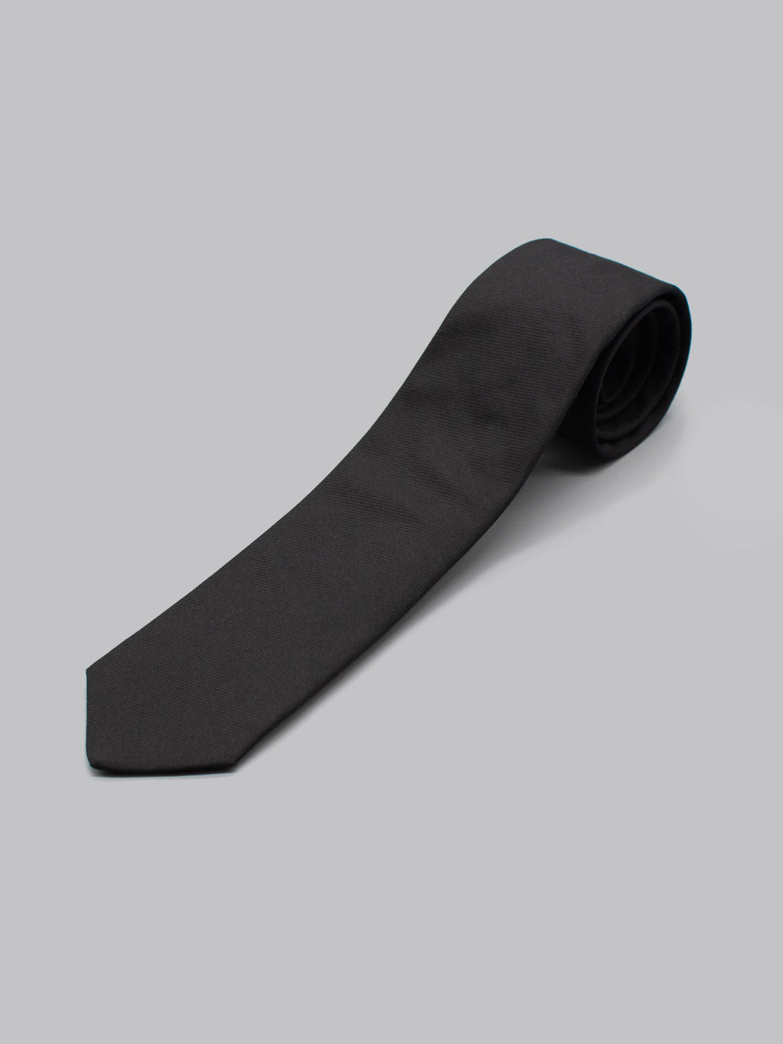 A Raven Black Cotton Tie by ID Menswear, handmade in Brooklyn from 100% cotton, is shown neatly rolled on a plain light gray background.