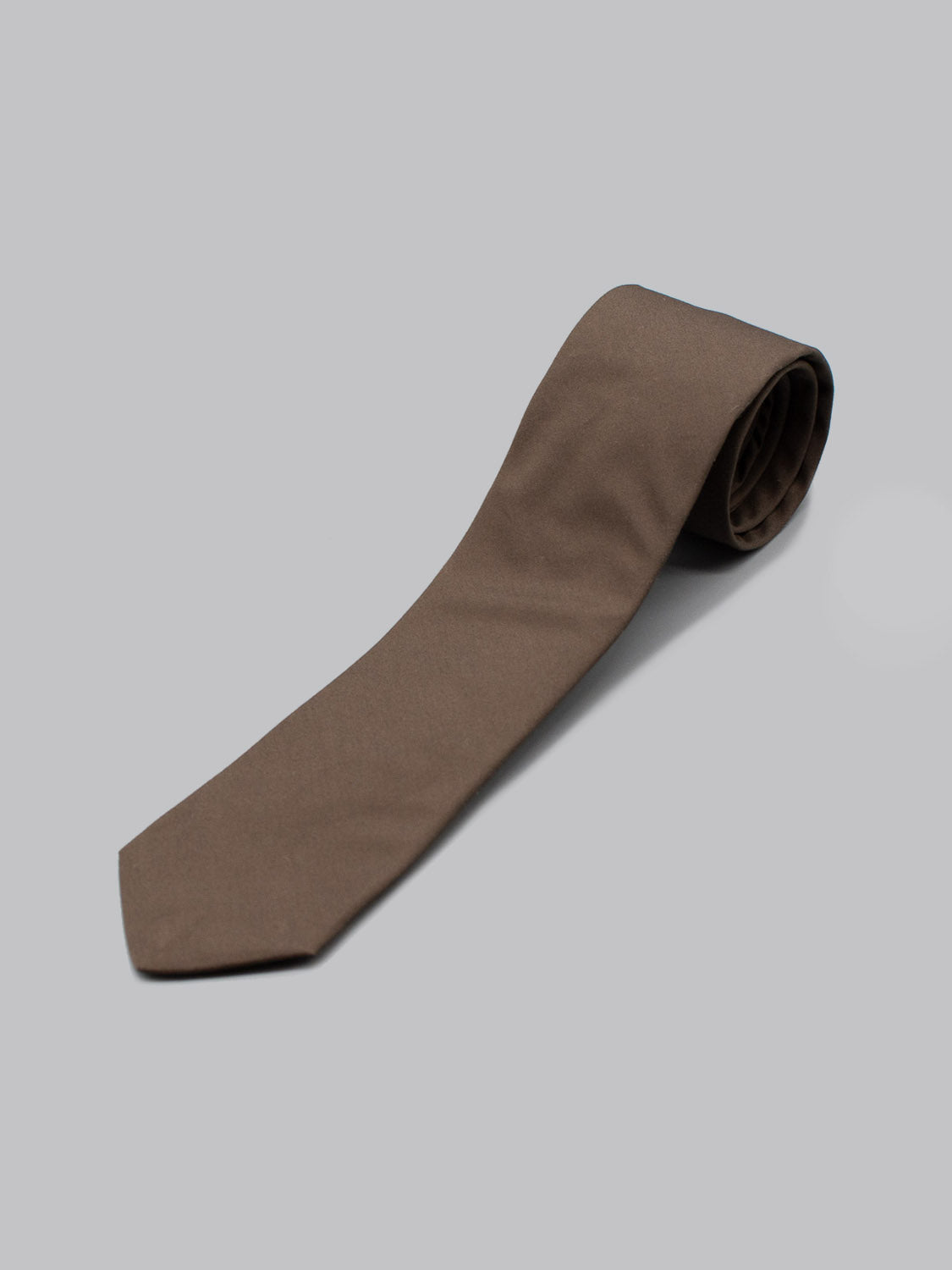 The Sparrow Cotton Tie by ID Menswear, handmade in Brooklyn in solid brown cotton, is rolled at one end and set on a plain light gray background—an ideal accessory for business formal attire.