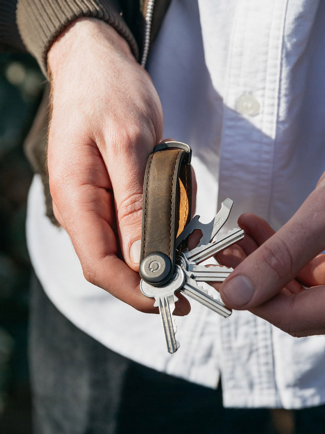A person in a white shirt and brown jacket fans out several keys and tools from the compact Orbitkeys Key Organizer Crazy-Horse Cowhide Leather.