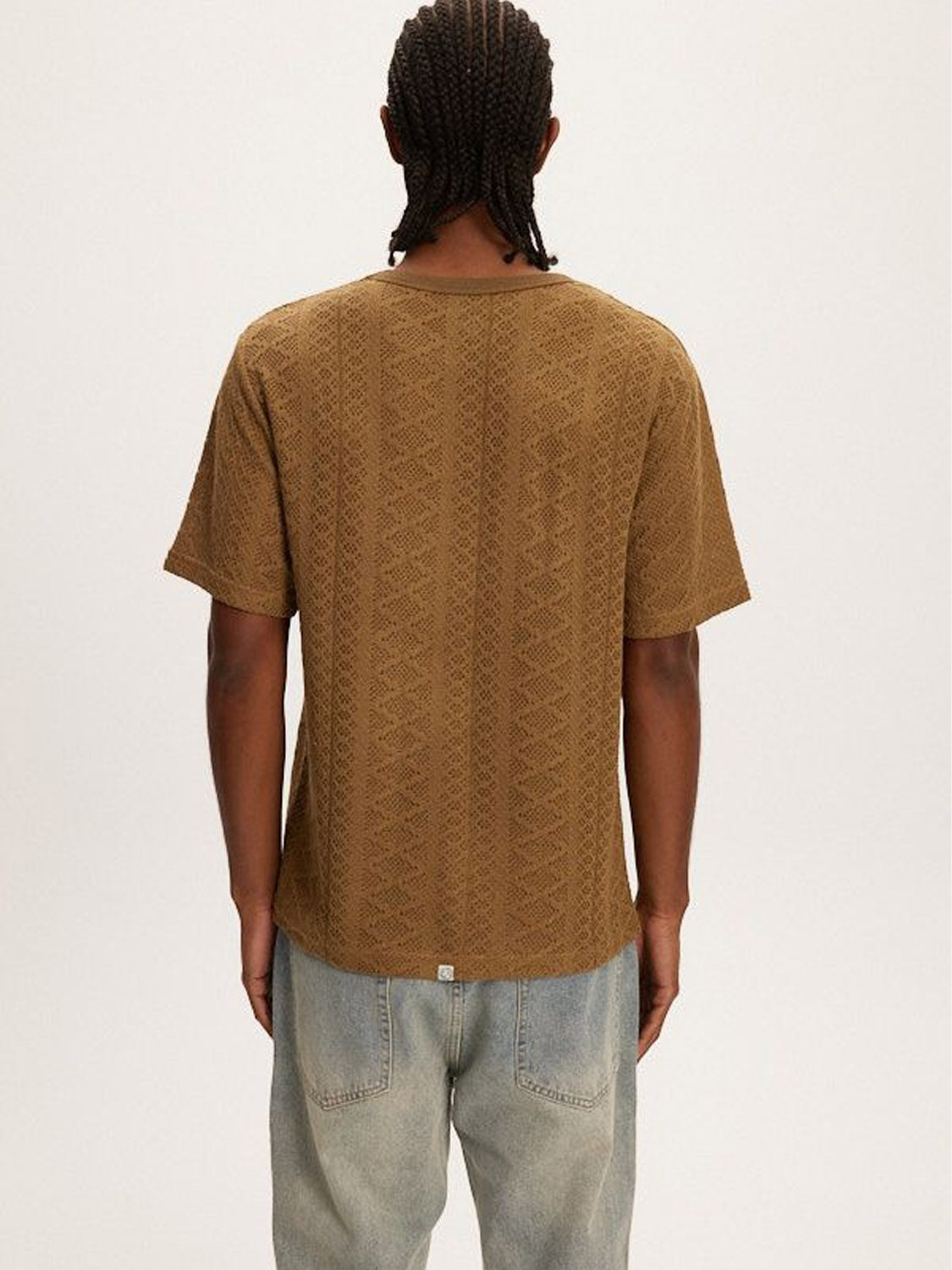Rear view of someone wearing the Kuwalla Crochet Jersey Tee, a classic fit brown patterned short-sleeve shirt, with light blue jeans against a plain background.