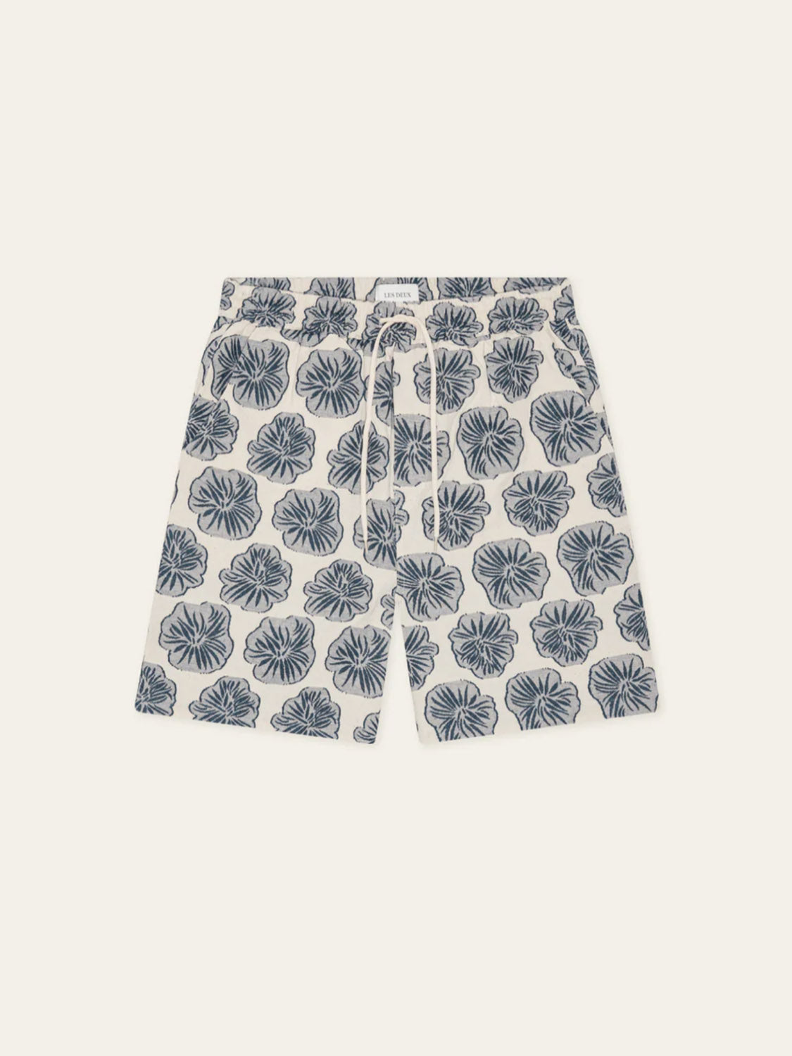 Les Deux Dahlia Jacquard Shorts are white cotton blend shorts with an elastic drawstring waist, featuring bold blue hibiscus flowers—a perfect laid-back summer style.