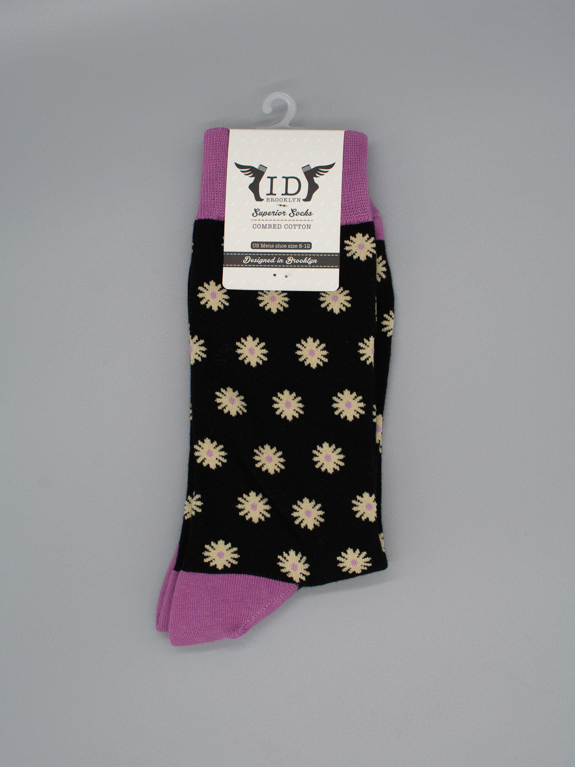 The Dazed Graphic Socks by ID Menswear feature black combed cotton with white and yellow daisies, plus purple cuffs, heels, and toes. Perfect for your modern wardrobe. Shown with a product tag at the top.