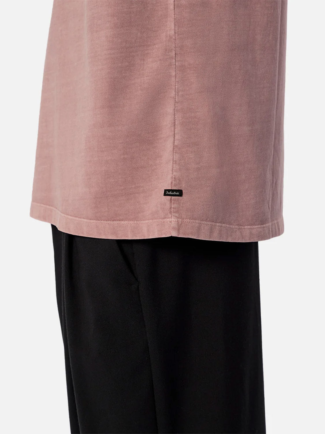 A side view shows a person wearing The Del Sur Tee by Industrie in light mauve, a relaxed fit crew neck with a small black label near the hem, paired with black pants against a plain background.