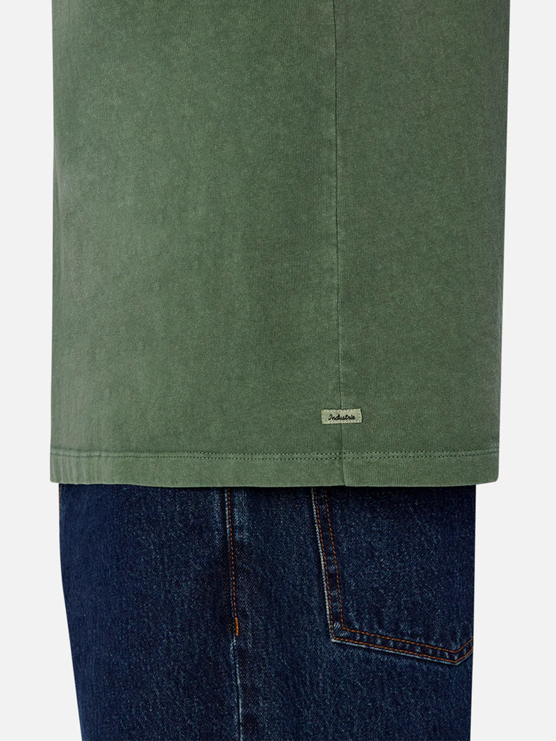 A person wears Industrie’s The Del Sur Tee in green, a relaxed fit crew neck with a visible small label on the hem, paired with dark blue denim jeans. Only the waist down is shown.