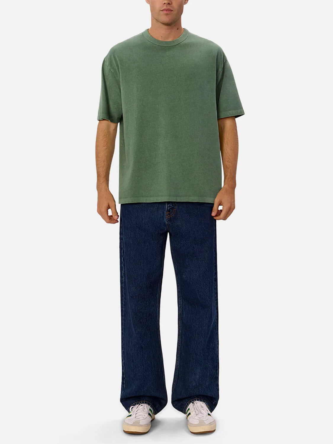 Someone wearing Industrie’s The Del Sur Tee—a relaxed fit, 100% cotton green crew neck—paired with wide-leg dark blue jeans and white sneakers stands against a plain light gray background.