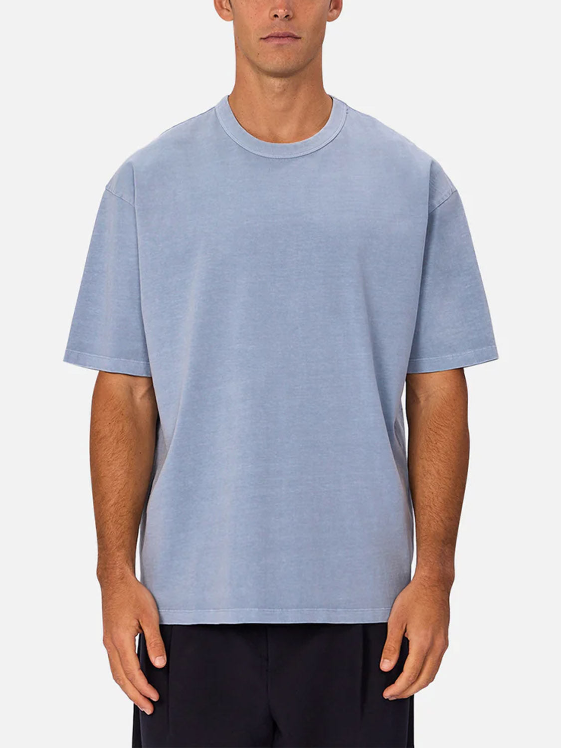 A man stands facing forward against a plain white background, wearing Industrie’s The Del Sur Tee in light blue 100% cotton and black shorts.