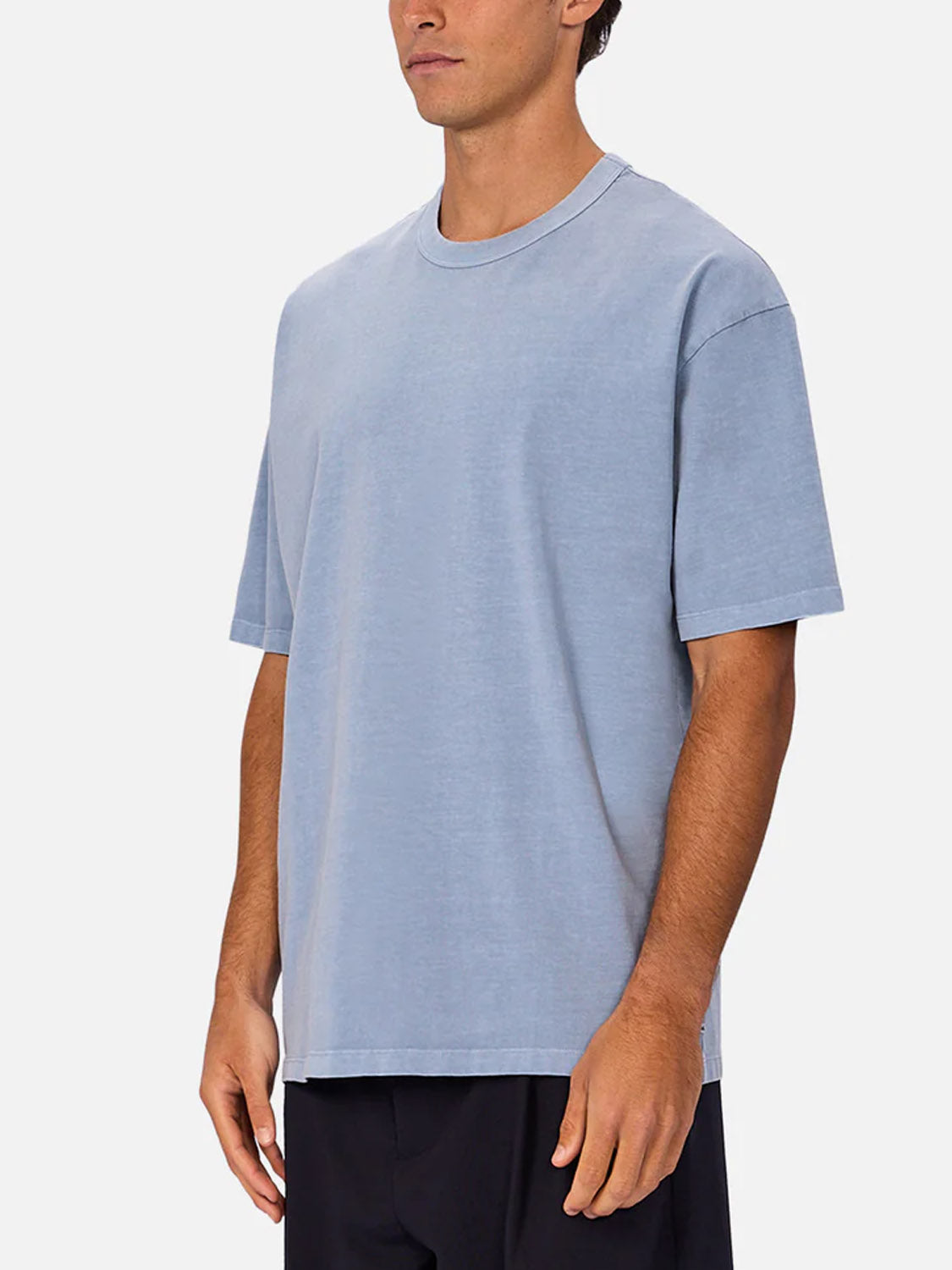A man stands against a plain white background wearing Industrie’s The Del Sur Tee, a loose-fitting light blue 100% cotton crew neck t-shirt, paired with black shorts.