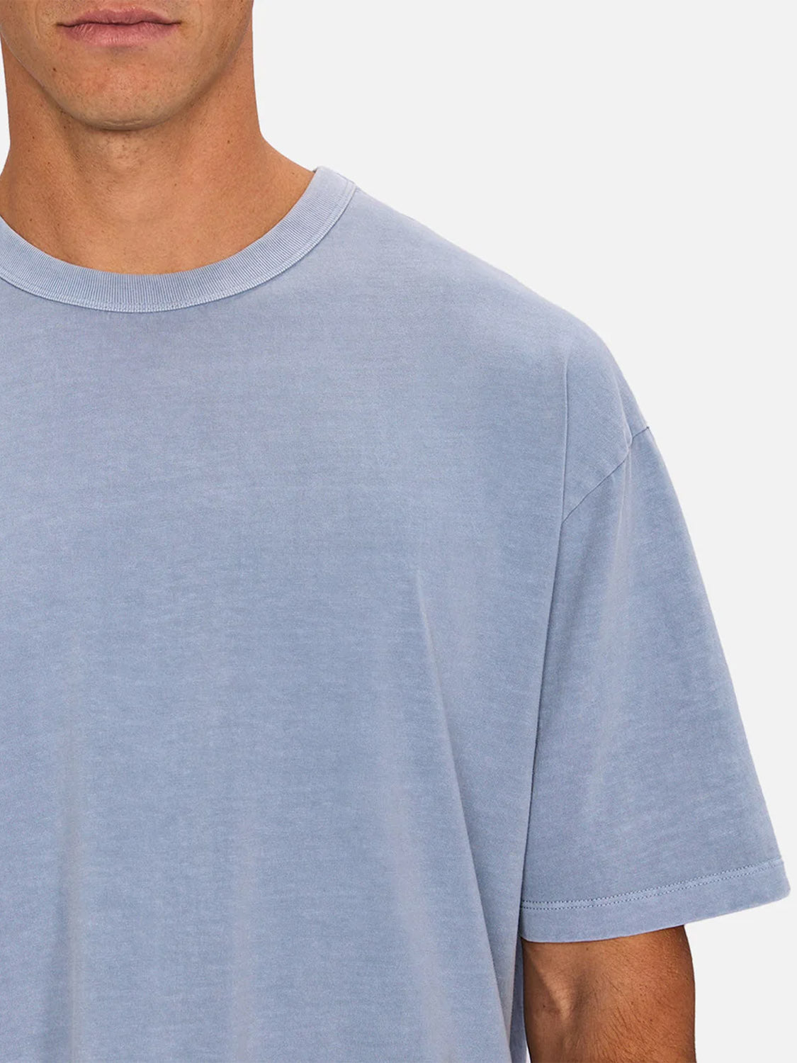 A person is shown from shoulders to mid-chest against a plain background, wearing Industrie’s The Del Sur Tee in light blue with short sleeves and a crew neck; only the lower half of their face is visible.