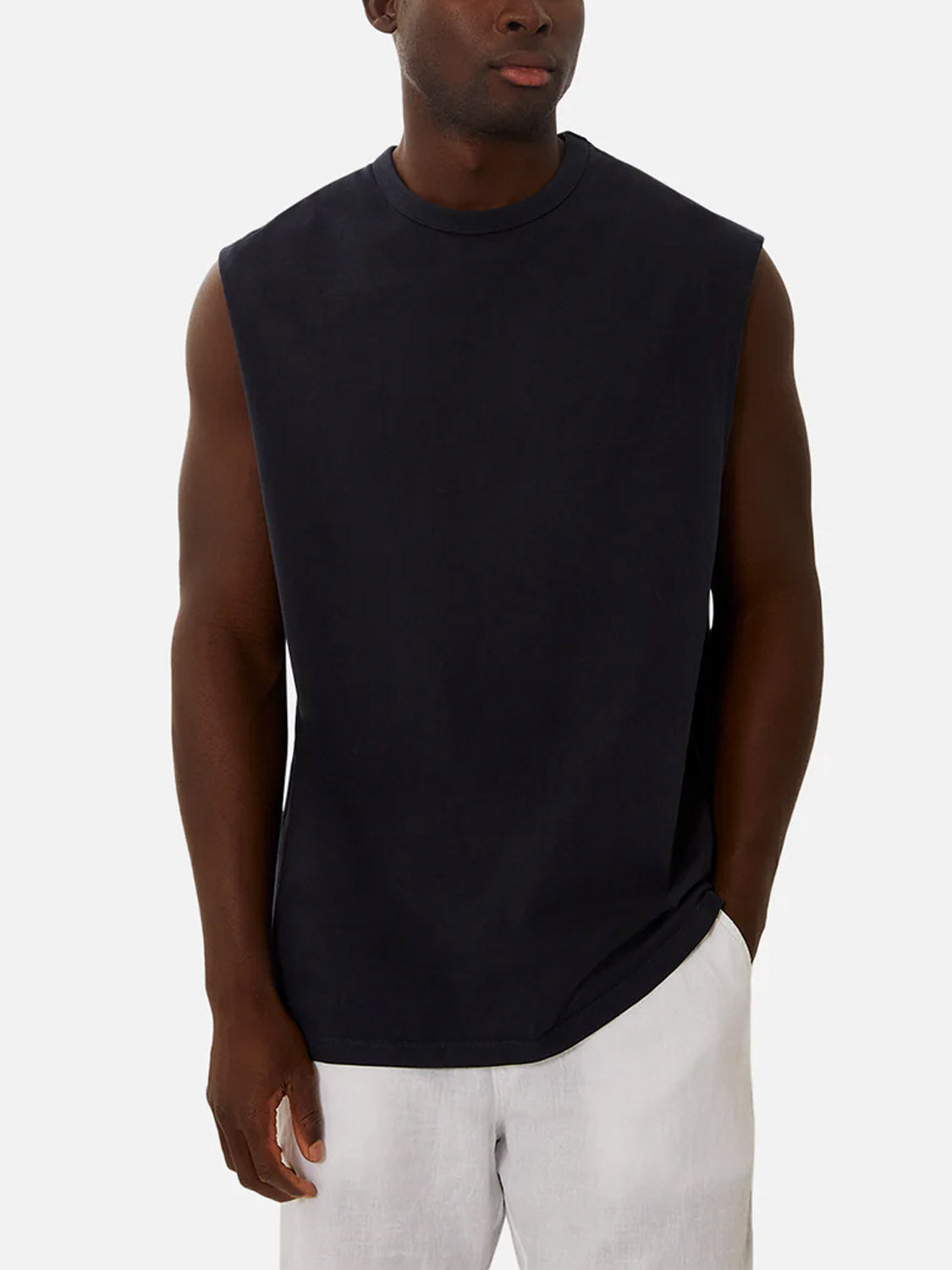 A man wears the Industrie Del Sur Sleeveless T-Shirt in black with light pants, standing with one hand in his pocket against a plain light background.