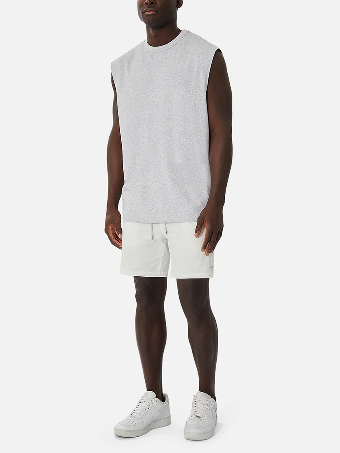 A man stands against a plain white background wearing the Industrie Del Sur Sleeveless T-Shirt in gray, paired with light gray shorts and white sneakers.
