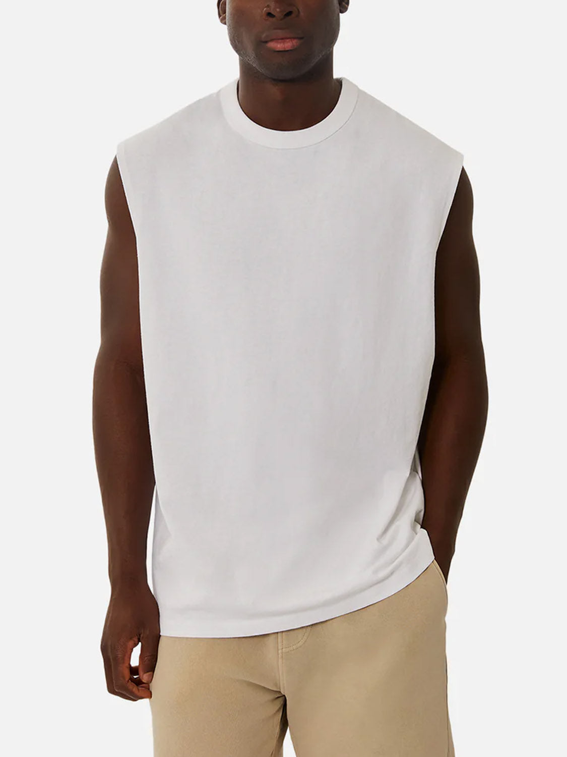 Wearing the Industrie Del Sur Sleeveless T-Shirt in white and light beige shorts, a person stands with one hand in their pocket against a plain white background.