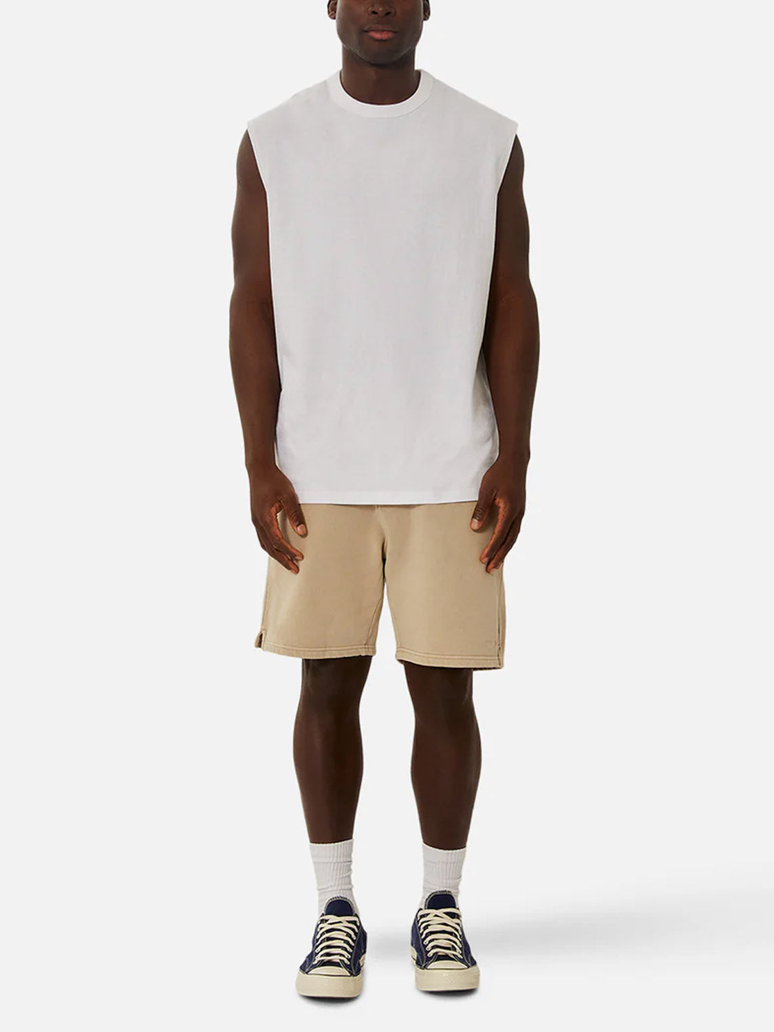 Someone wears the Industrie Del Sur Sleeveless T-Shirt in white, paired with beige shorts, white socks, and navy blue sneakers, standing against a plain white background.