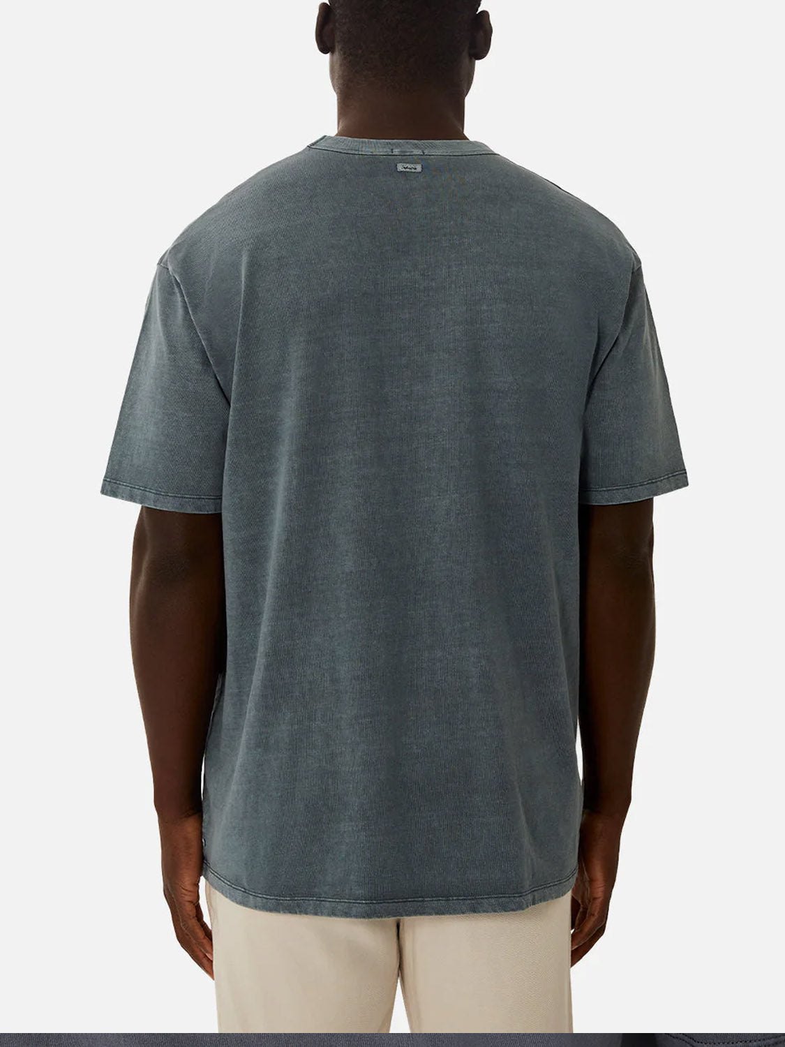 A person is shown from the back wearing Industrie’s The Del Sur Tee—a relaxed fit, faded dark gray 100% cotton crew neck—paired with light-colored pants, standing against a plain white background.